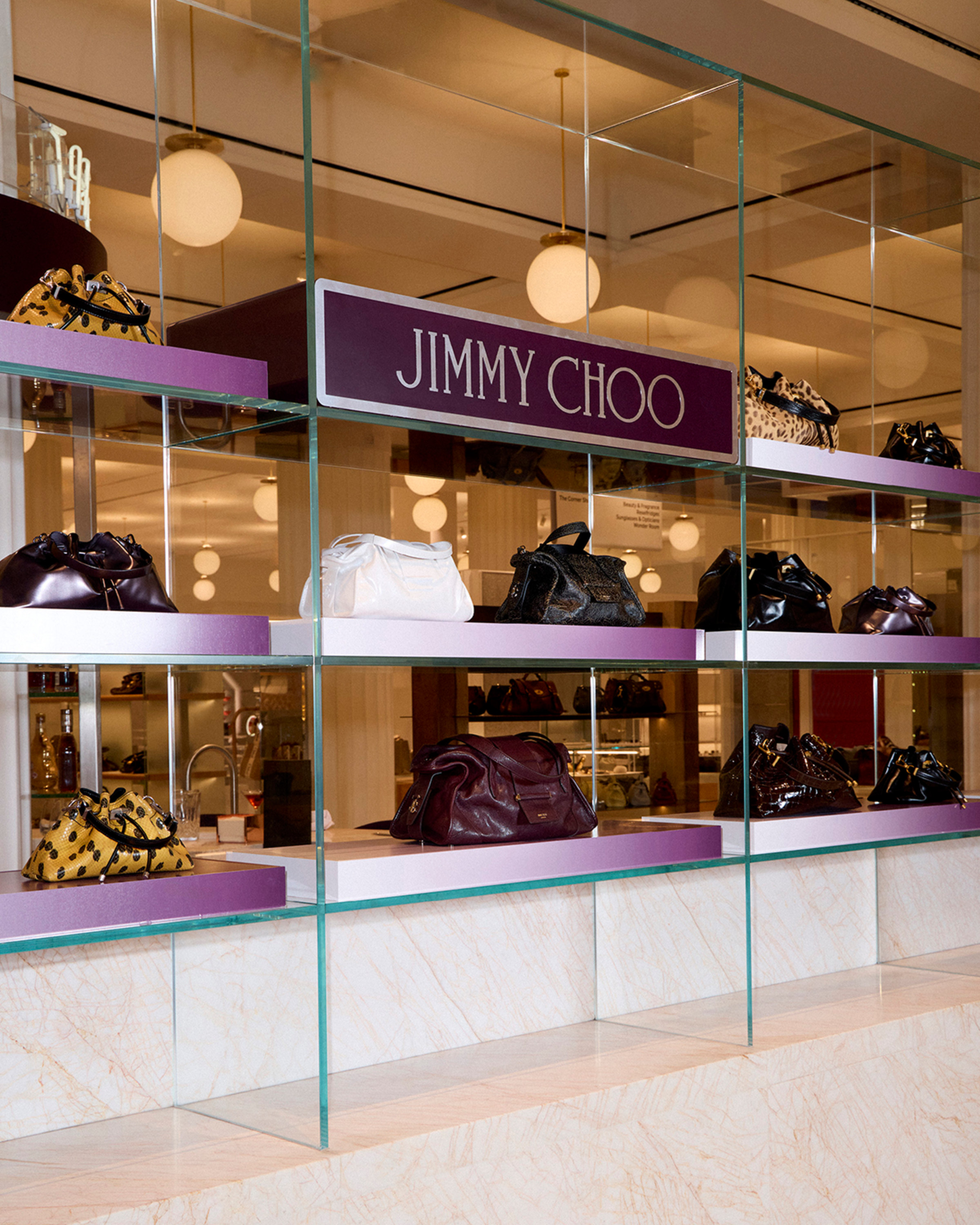 Jimmy Choo handbag display at Selfridges, featuring bags arranged on glass shelving with purple detailing.