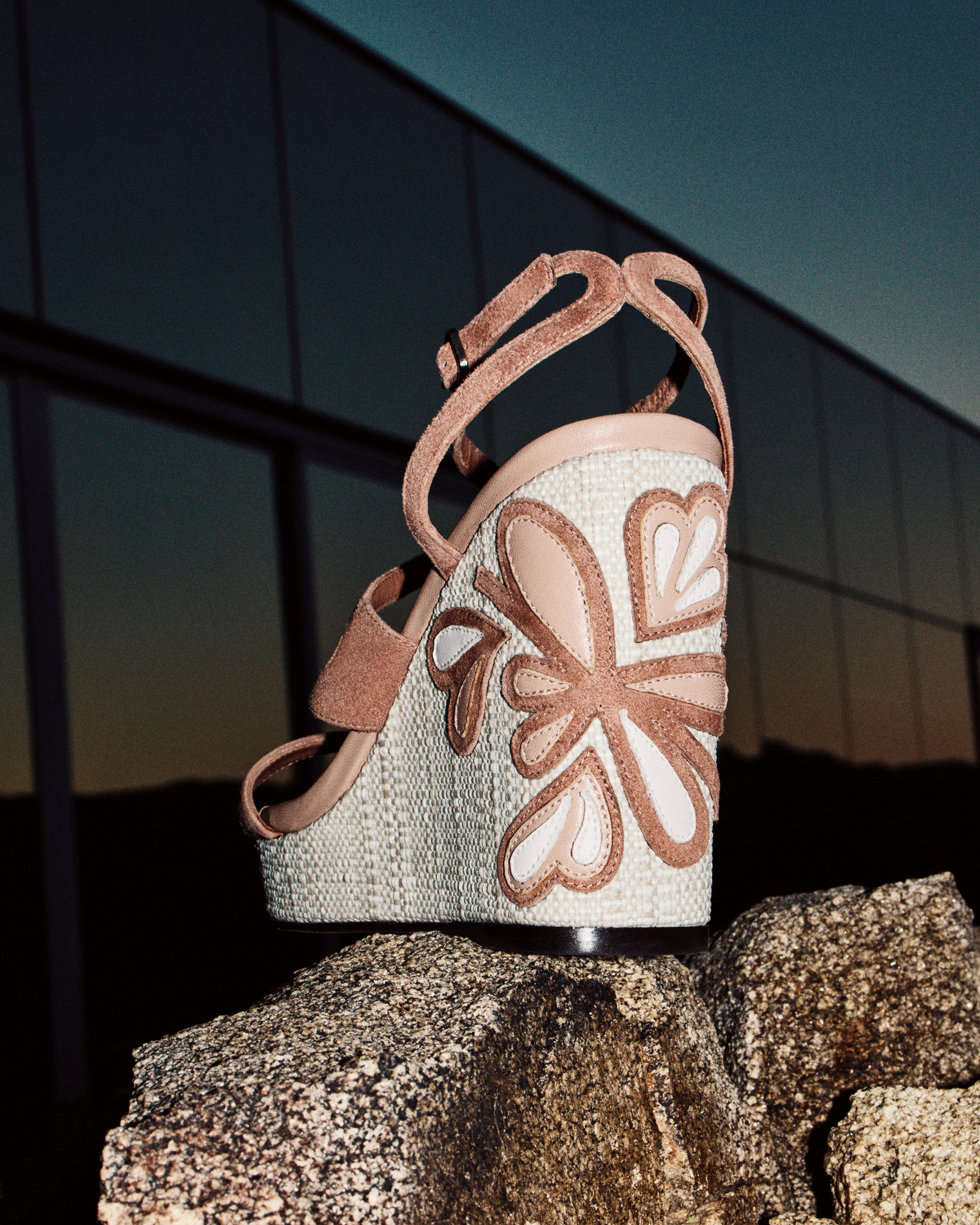 Transparent glitter jelly sandal with sculptural heel casting a shadow in sunlight.
