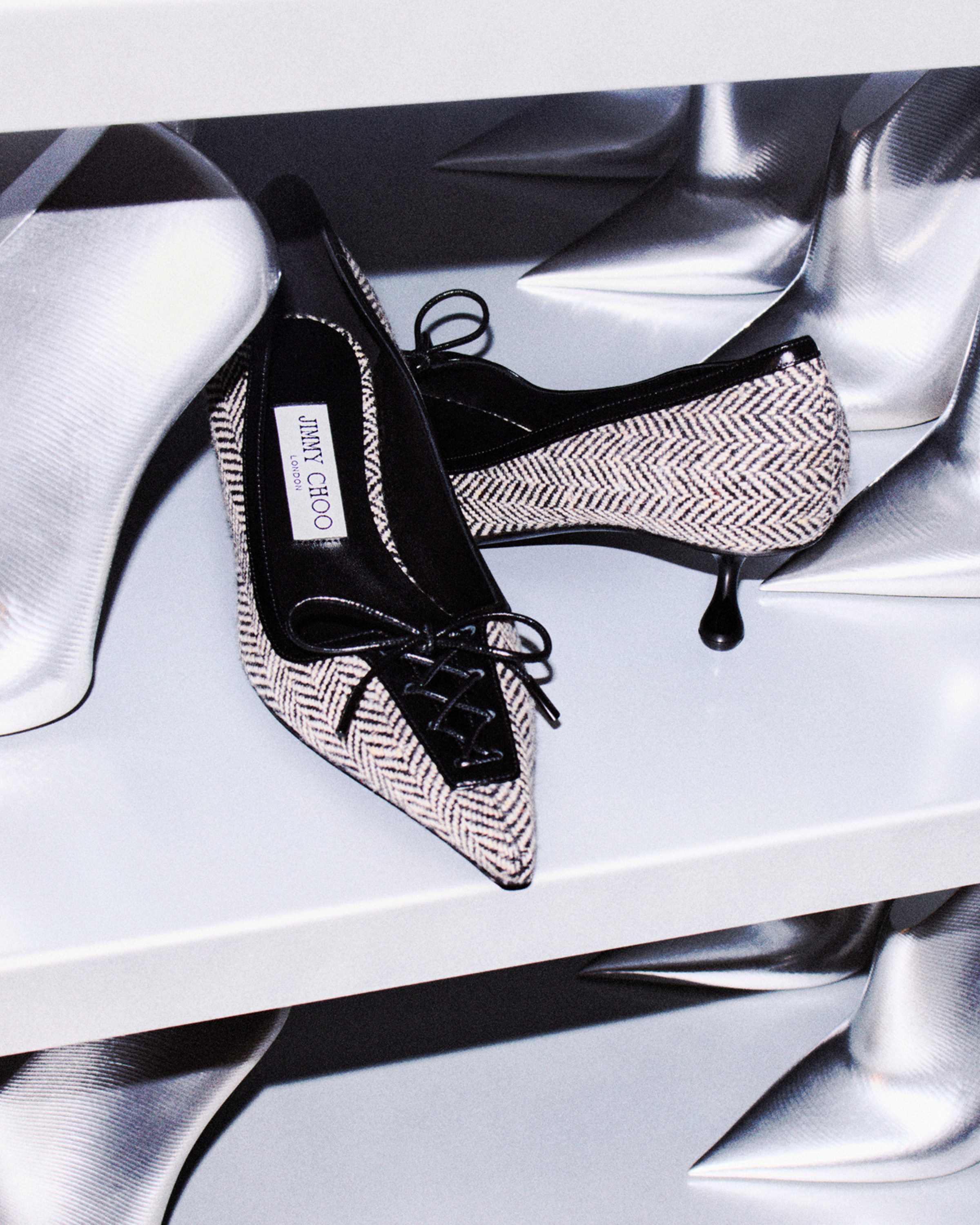 Close-up of a black leather pointed-toe pump with a knotted bow detail, worn with sheer tights. Photographed on stone surface.