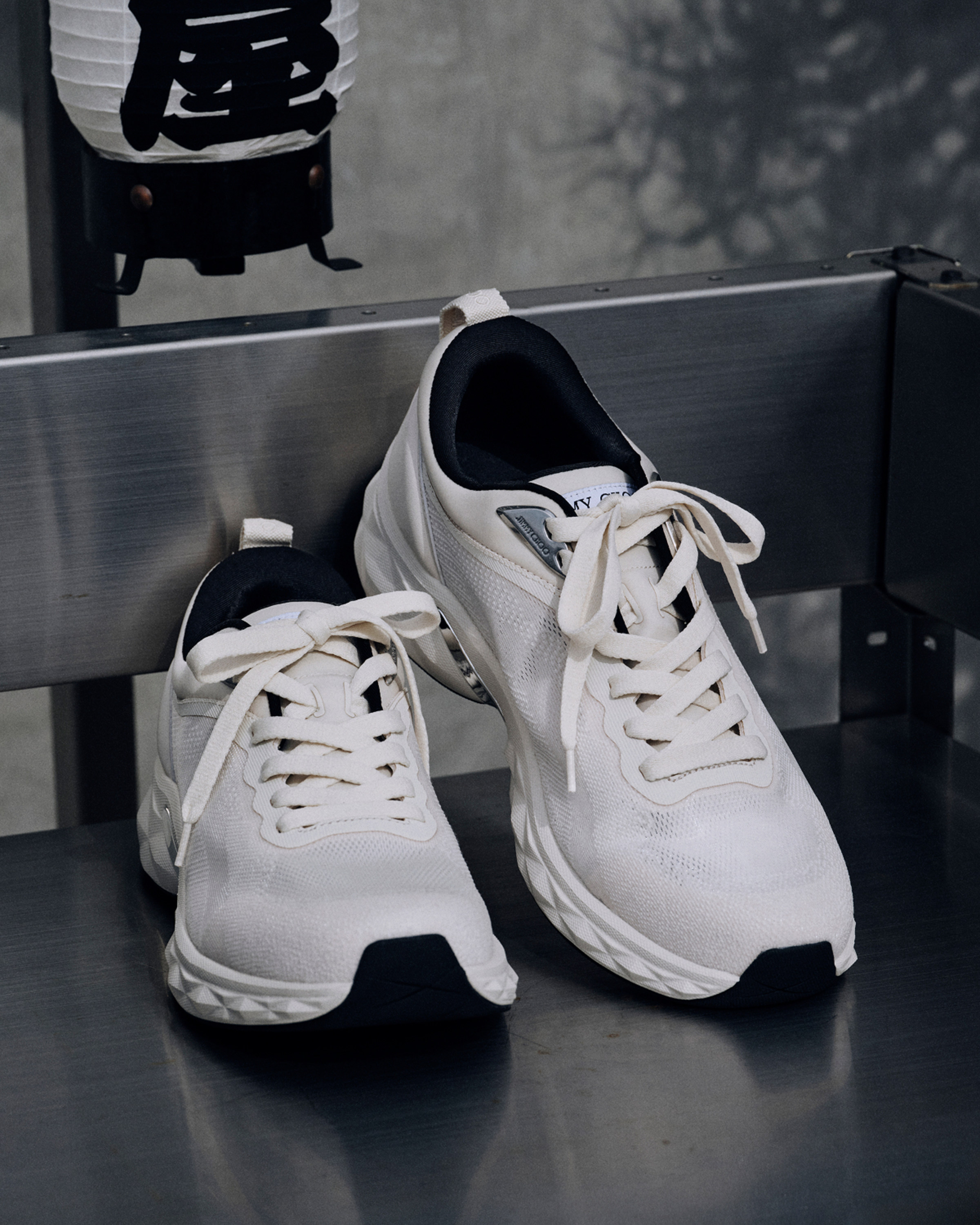 White lace-up trainers with black sole detail, placed on a metal bench.			