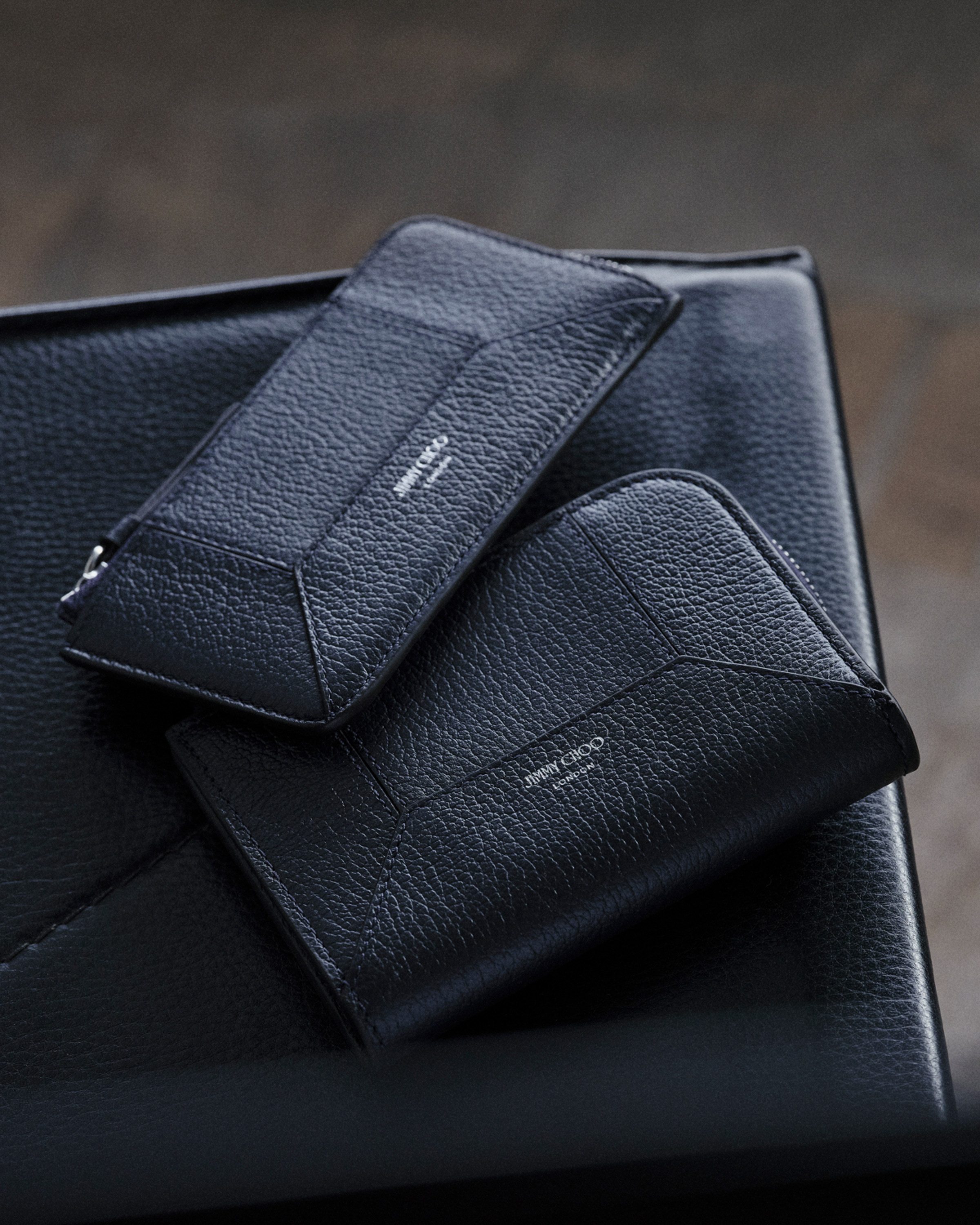 Black leather card holder and wallet with textured finish placed on a leather surface.