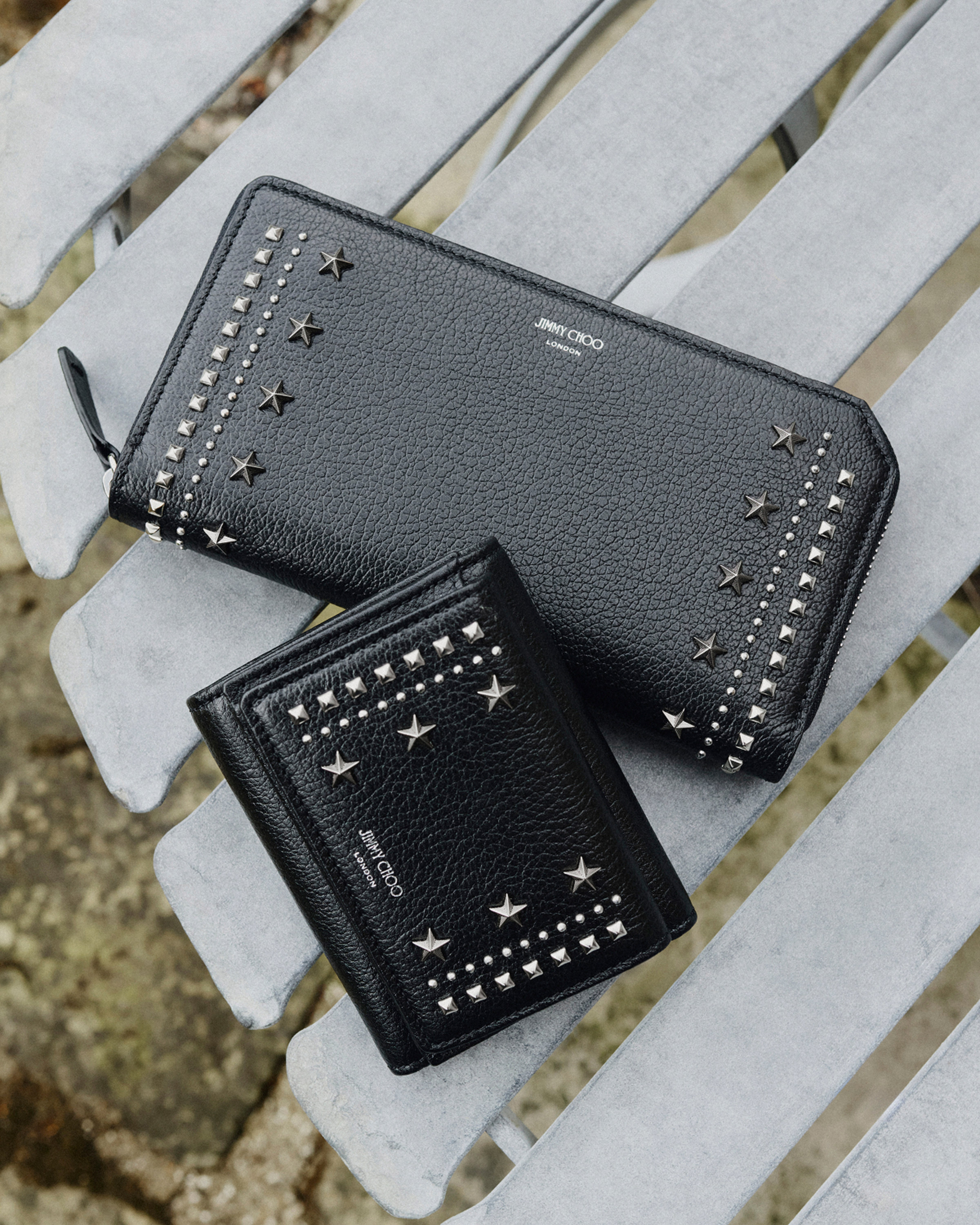 Black leather zip-around wallet with star and stud detailing placed in grass beside small purple flowers.