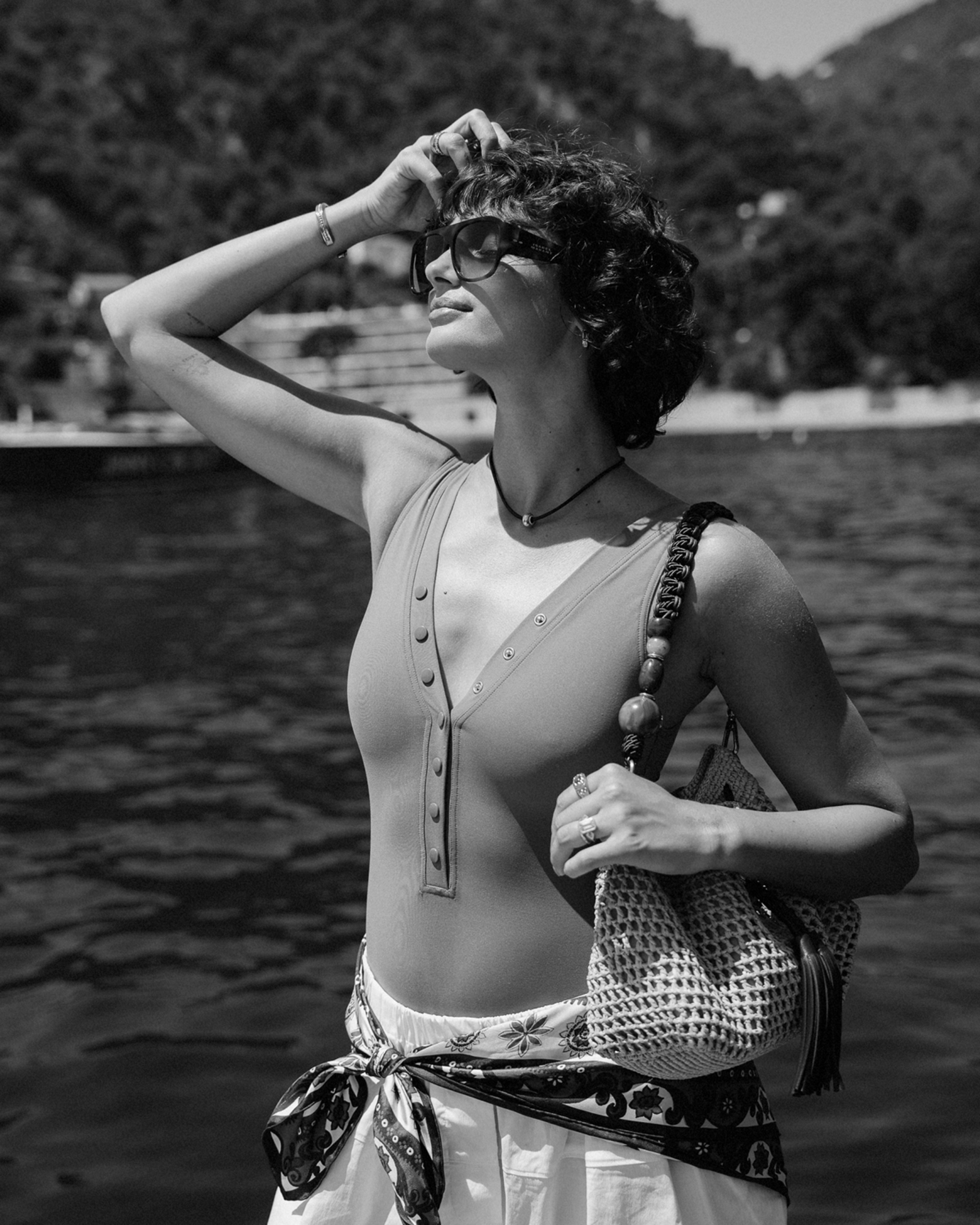 Black and white portrait of a woman wearing sunglasses and carrying a woven and beaded shoulder bag.