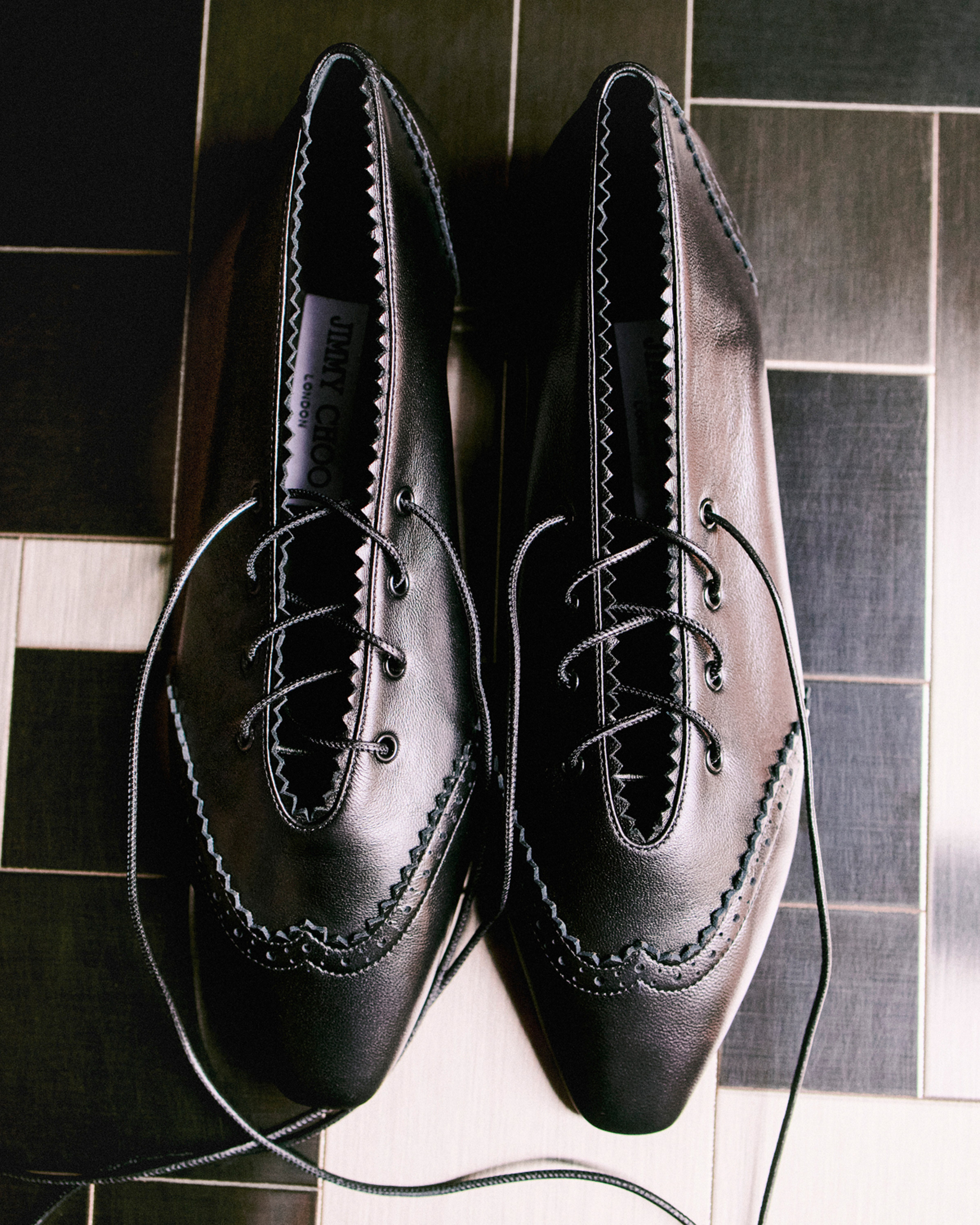 Pair of black leather pointed-toe lace-up pumps displayed on a tiled surface.