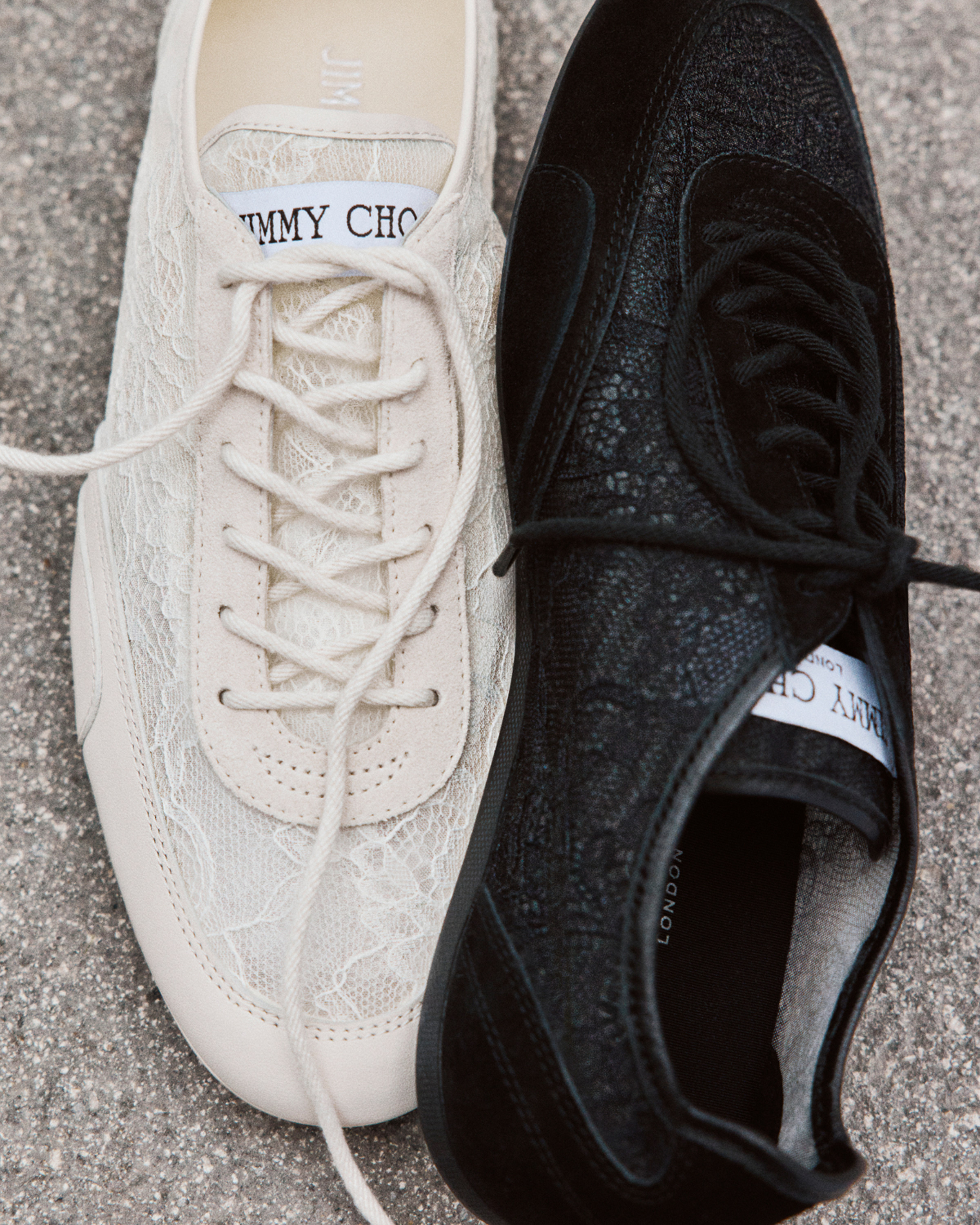 Cream lace low-top trainer displayed beside a black trainer on a stone surface.