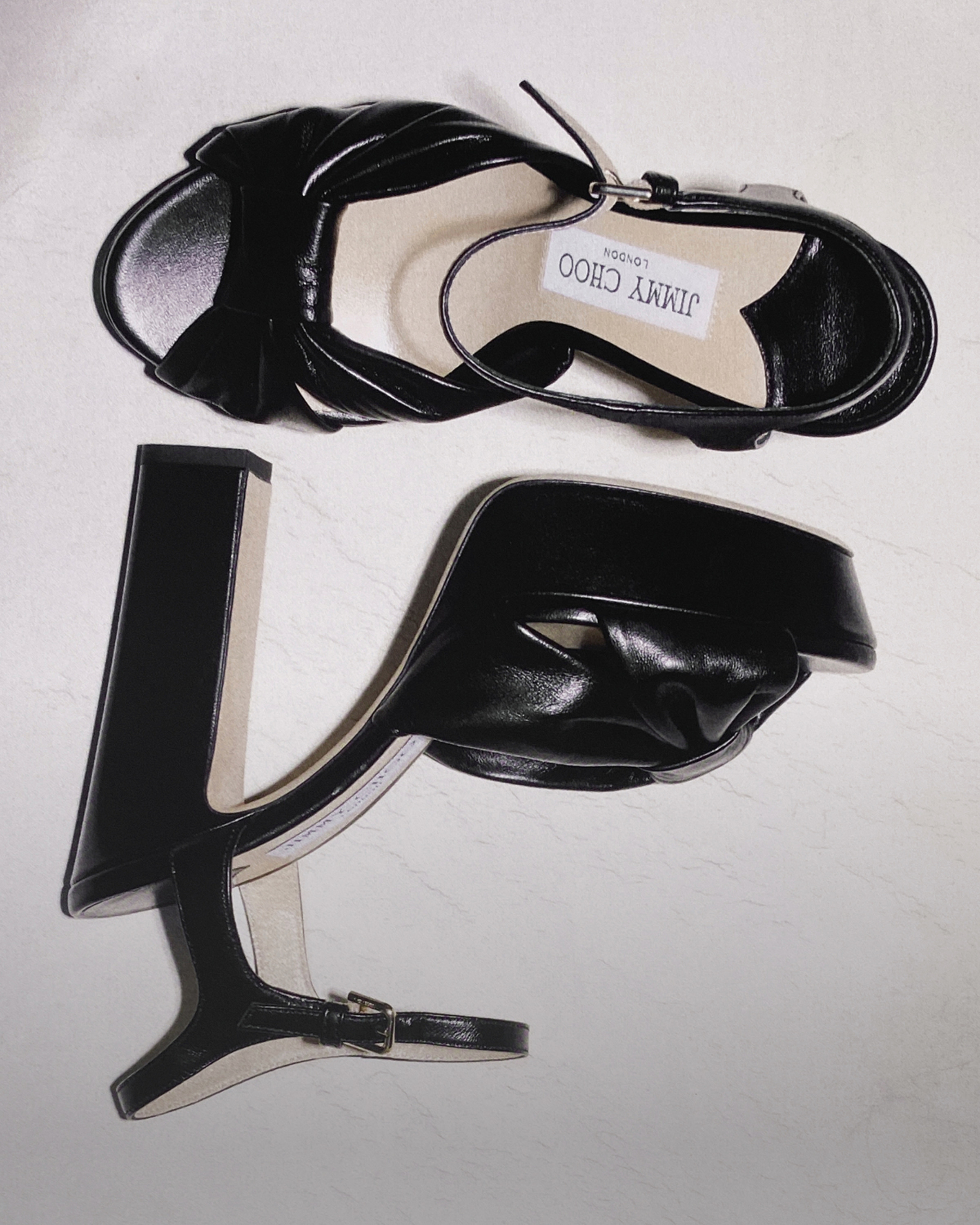 Black patent leather platform sandals with sculptural block heels and knot detail displayed from above.