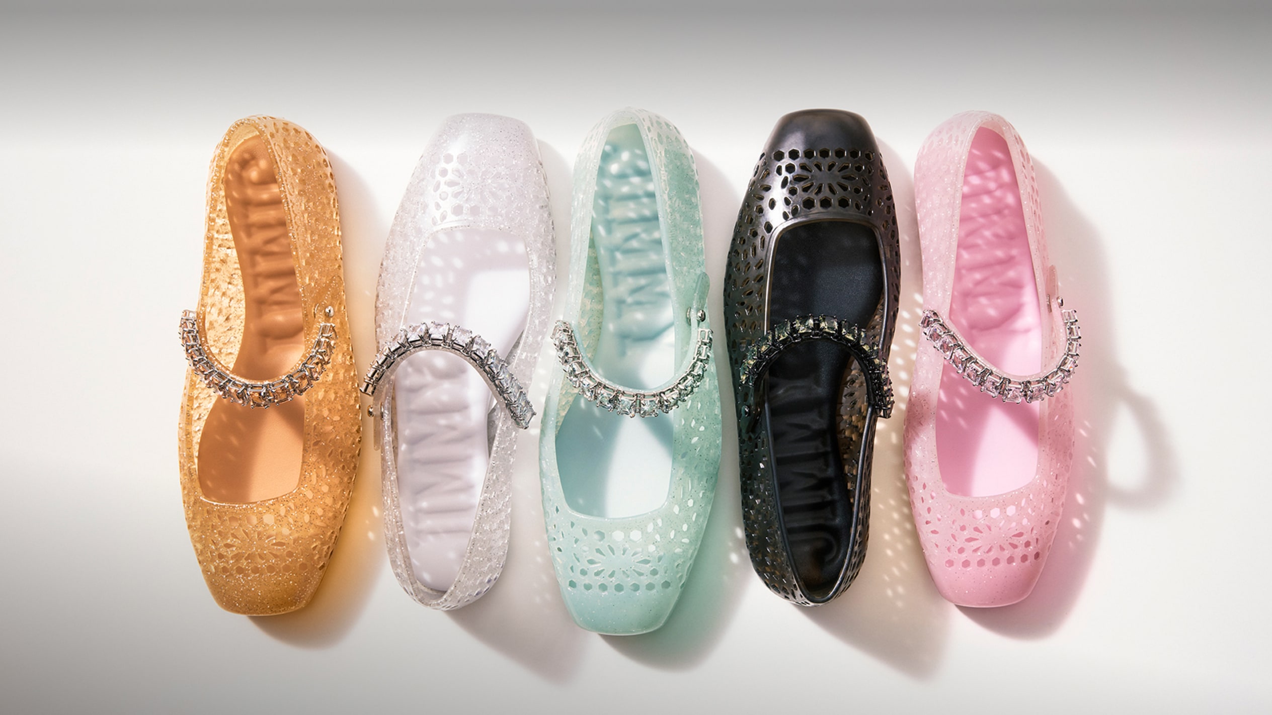 Colourful ballet flats with crystal strap detail arranged side by side on a neutral background.