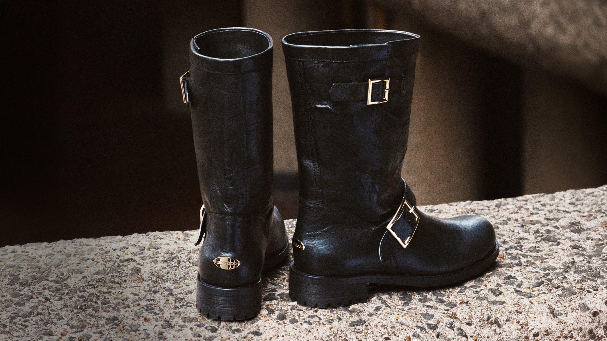 A lineup of Jimmy Choo Sunny trainers arranged side-by-side on a light surface, featuring lace-detailed uppers in latte, black, and yellow tones.