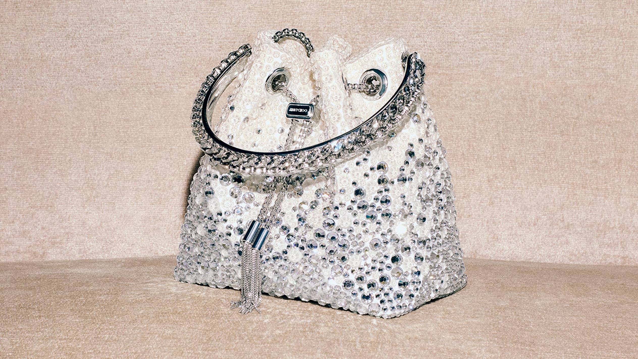 Close-up of a sparkling pointed-toe pump embellished with crystals and a delicate ankle strap, set against a soft green background.