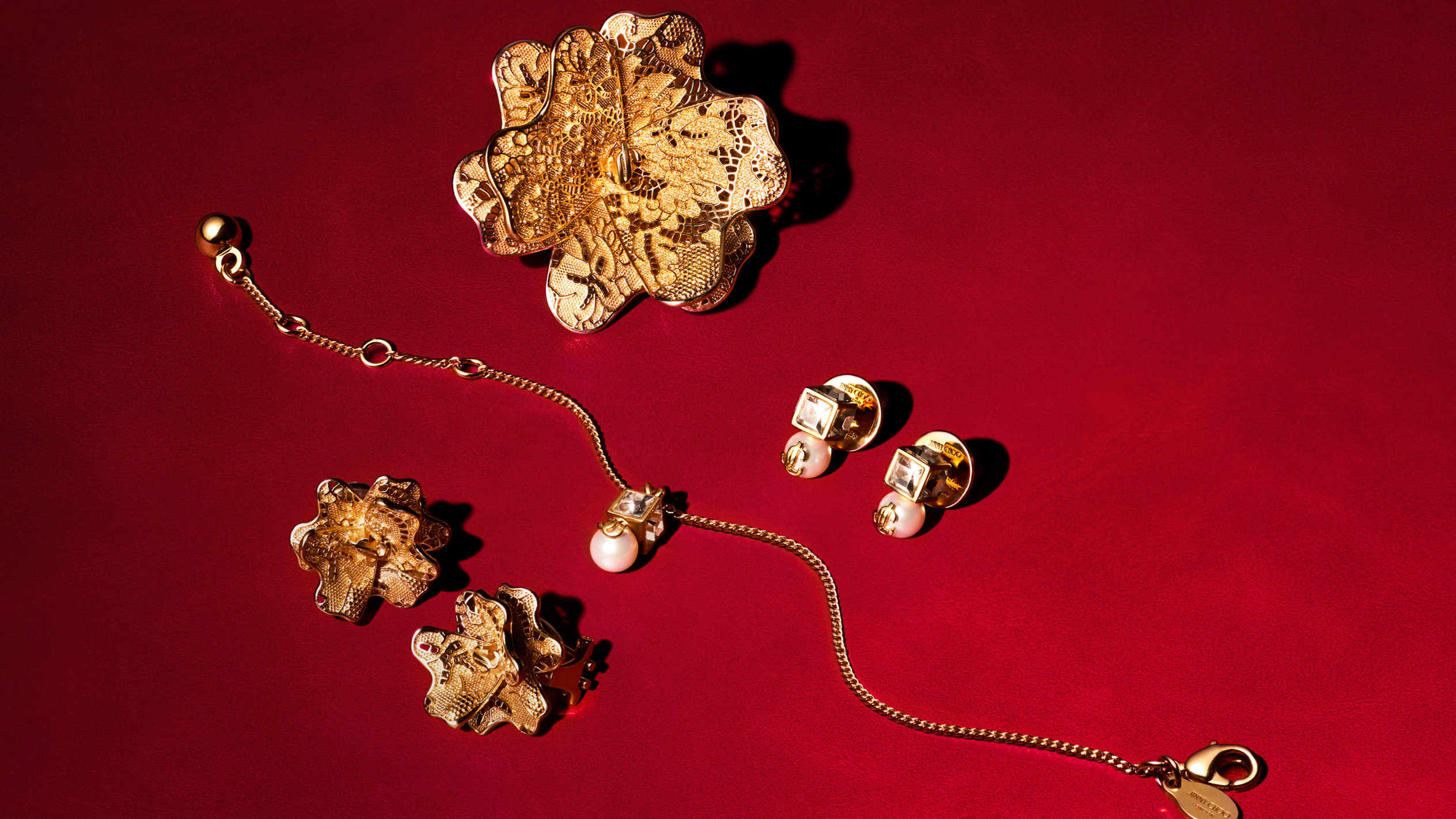 白地にゴールドの縁取りのエレガントなプレートに並べられた、ピアスやパール付きブレスレットなどのゴールドのフラワーモチーフジュエリー。	