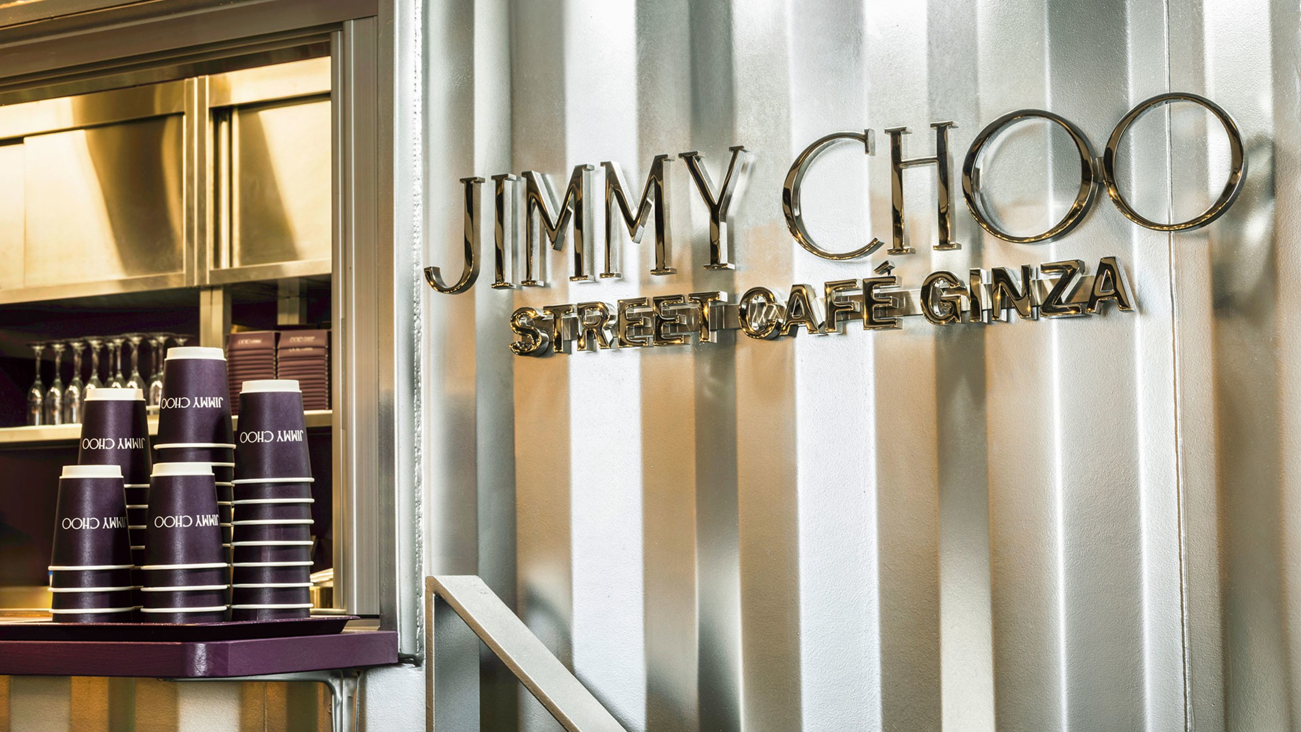 Woman standing outdoors wearing a white oufit, holding the Jimmy Choo Curve Bag in light leather with gold hardware.