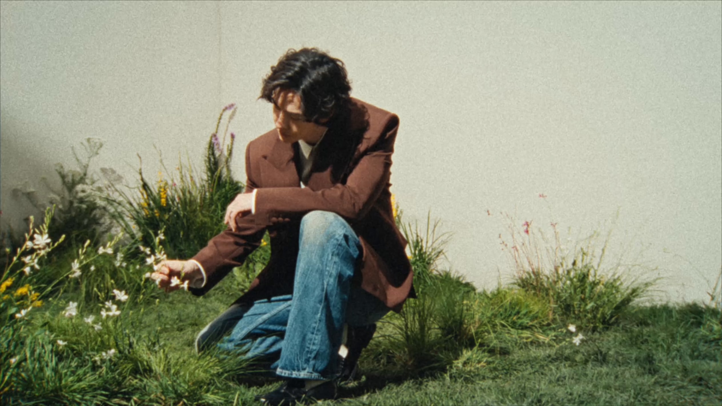 IMAGE ALT: Model crouching by a window holding a multicolour woven drawstring bag with desert rocks in the background.