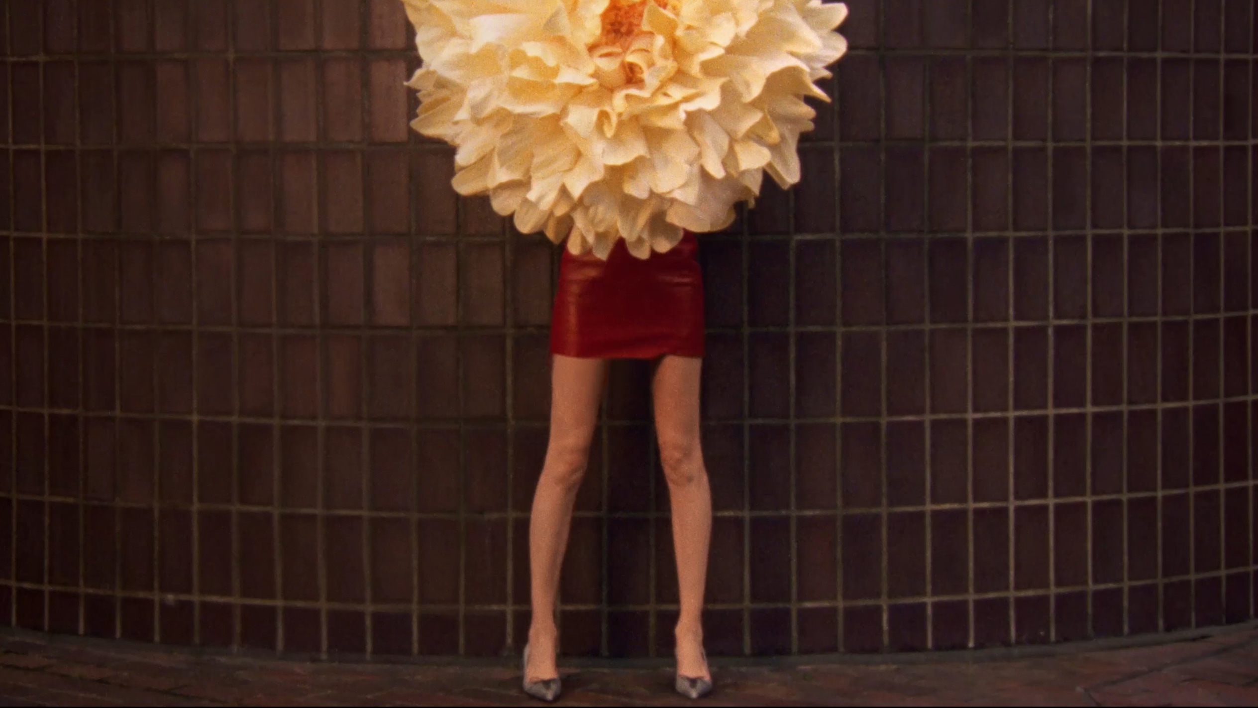 Pointed-toe pumps with corset detail worn with bare legs, styled while leaning on a brick wall.