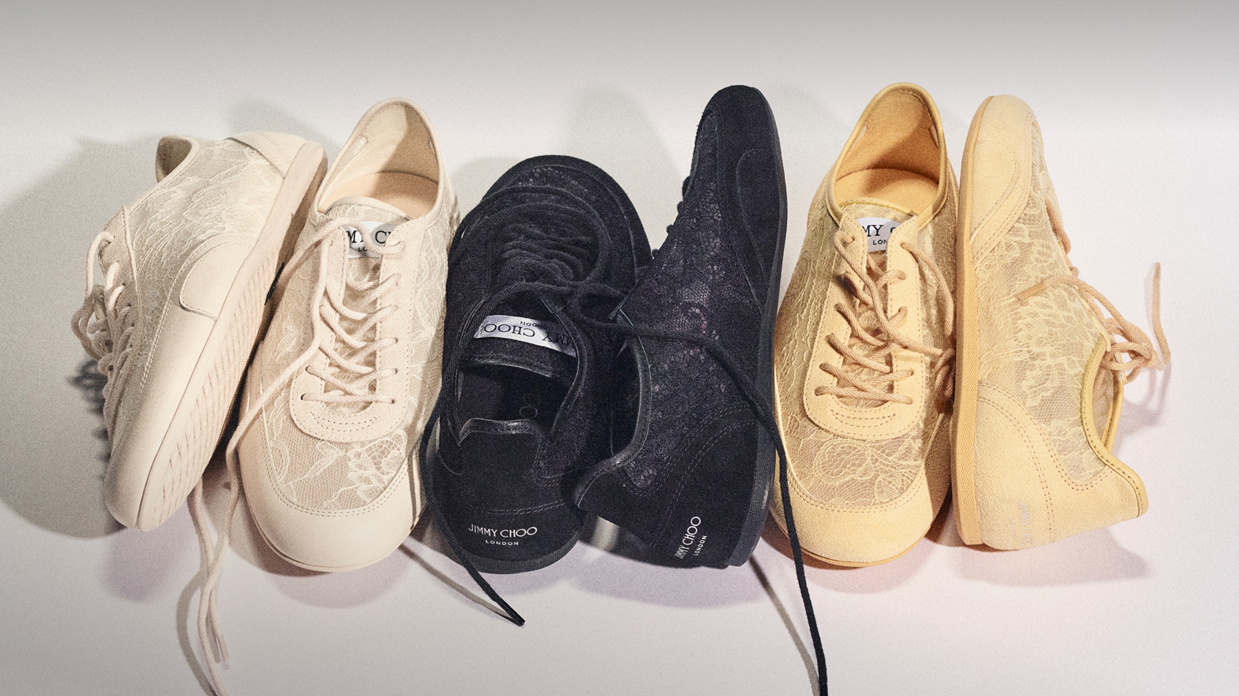 Selection of lace low-top trainers in cream, black and yellow tones arranged side by side.			