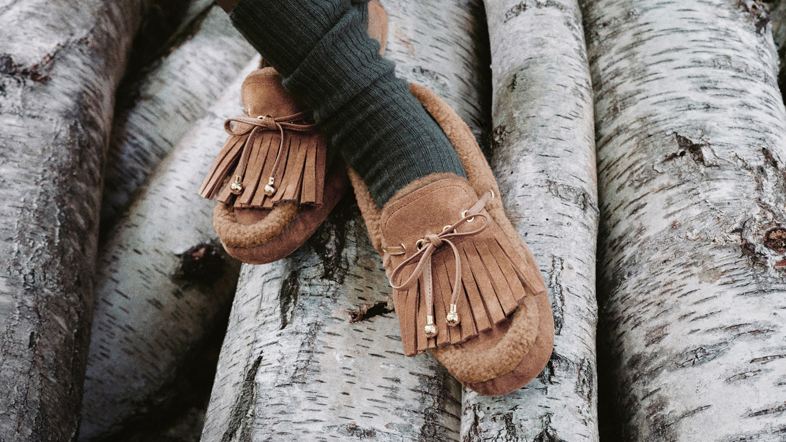  Brown leather ankle boot with chunky sole and cream cable-knit panel, photographed outdoors against a tree trunk in a forest setting.