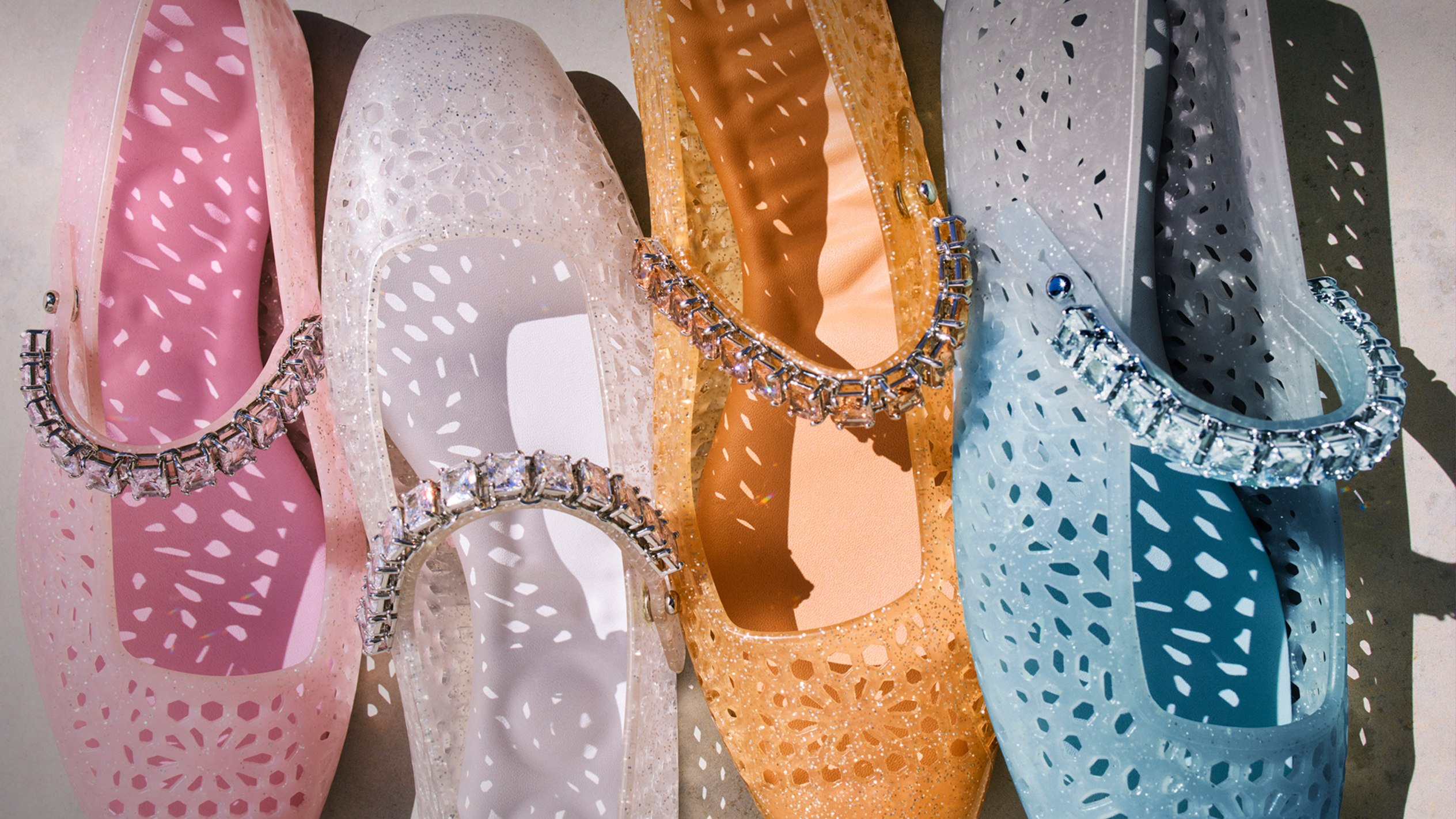Blue, amber, clear and pink jelly ballerina flats arranged side by side, each detailed with a crystal-embellished strap.