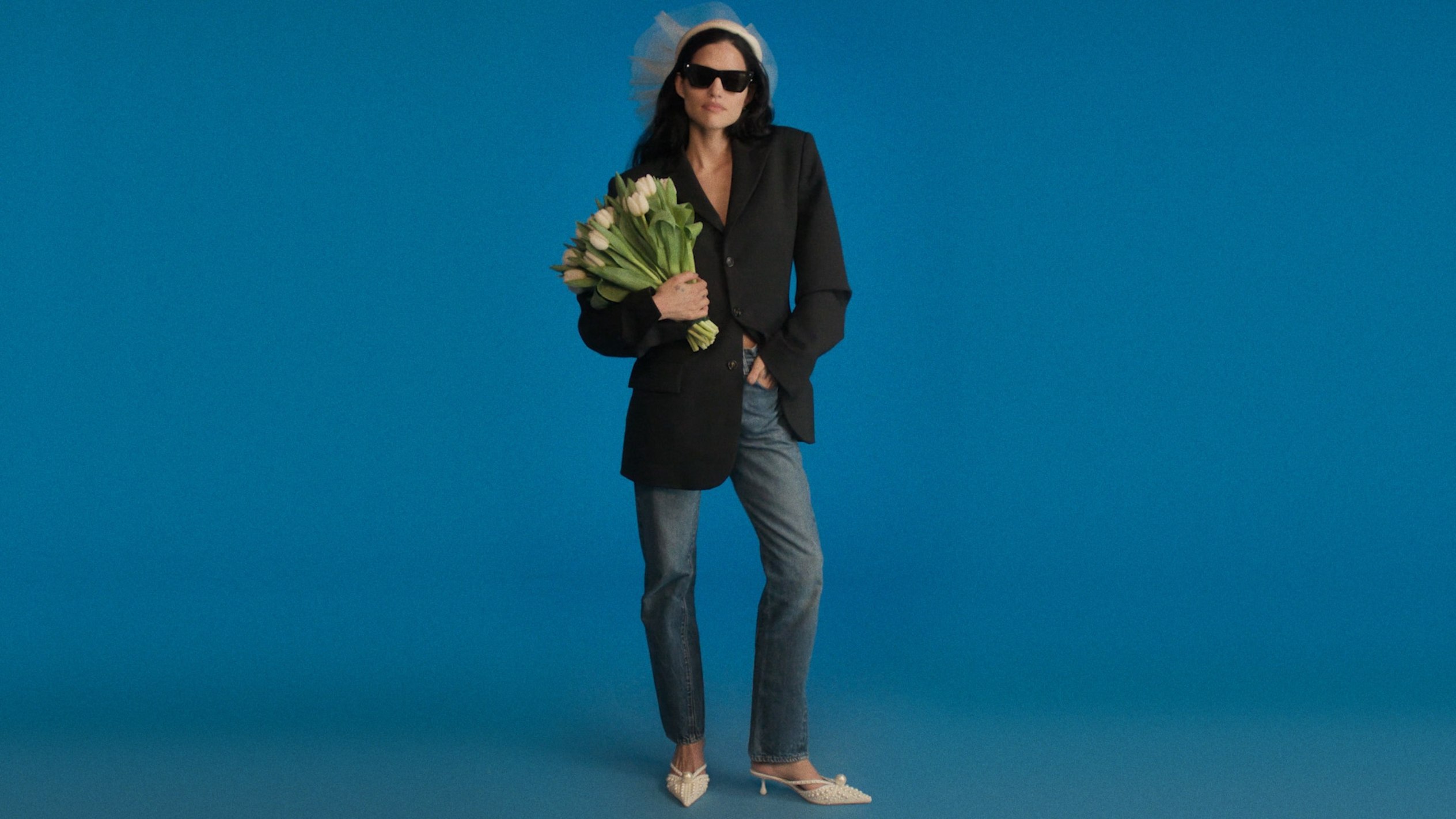  Model wearing ivory bridal heels with pearl detail, holding white flowers indoors