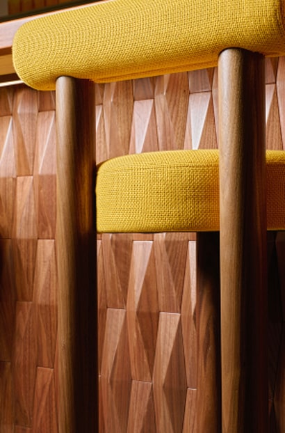 Close-up of a caf&eacute; table with yellow seating and a wooden tabletop holding a black menu and cutlery.