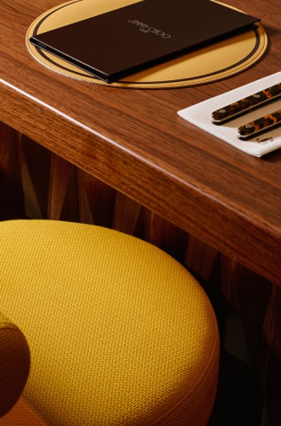 Close-up of a caf&eacute; table with yellow seating and a wooden tabletop holding a black menu and cutlery.