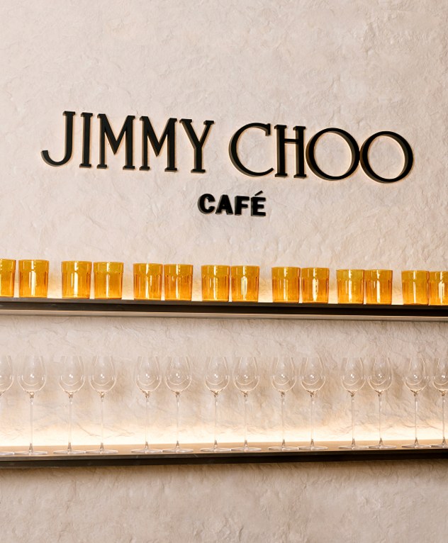  黄色いバースツールと照明付きの棚が特徴の Jimmy Choo Caf&eacute; の店内。
