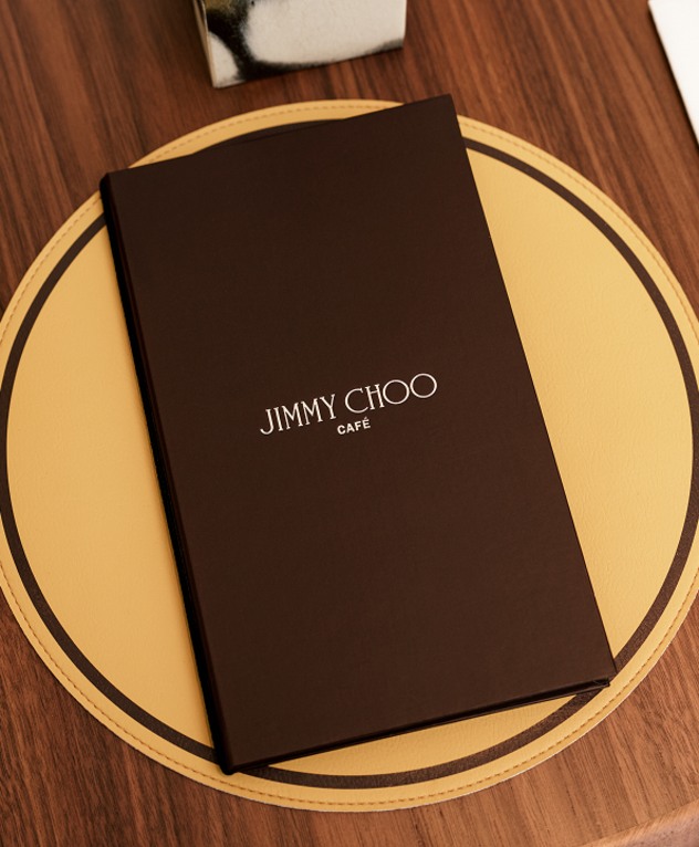 丸い黄色いテーブルの上に置かれた黒い Jimmy Choo カフェメニューのクローズアップ。 