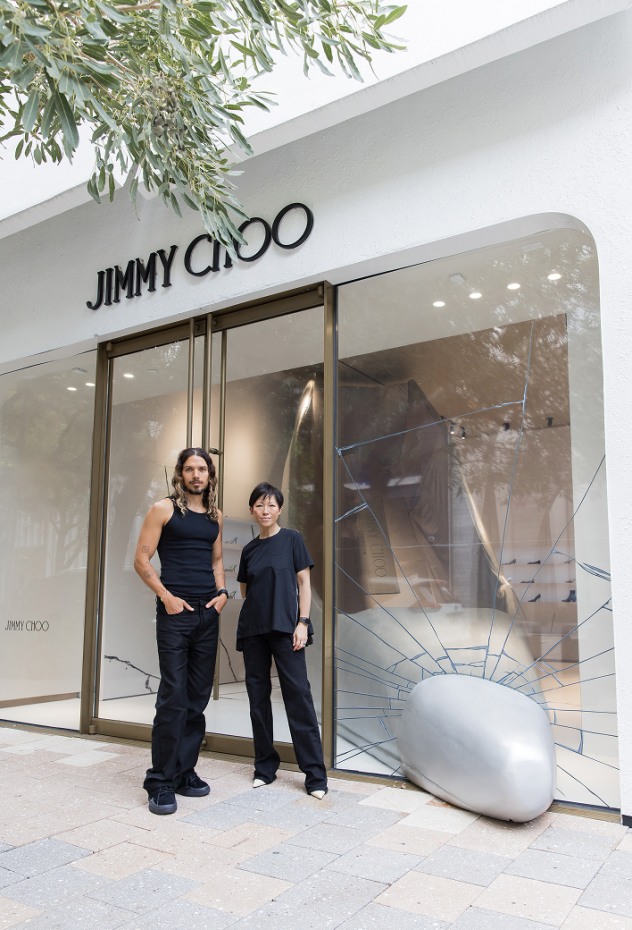 Exterior of the Jimmy Choo boutique with a large silver high-heel sculpture breaking through the front window, with Sandra Choi and Harry Nuriev standing outside the entrance.