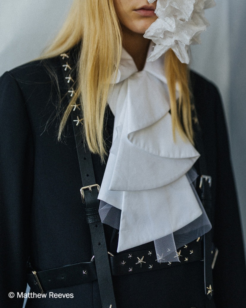 Close-up of black tailoring with ruffled white shirt and star-studded leather harness.