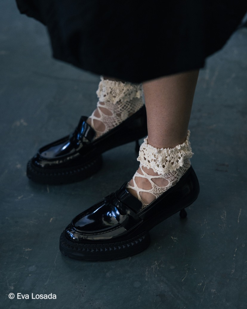 Black leather platform loafers worn with mesh socks and white ruffled skirt, photographed backstage.