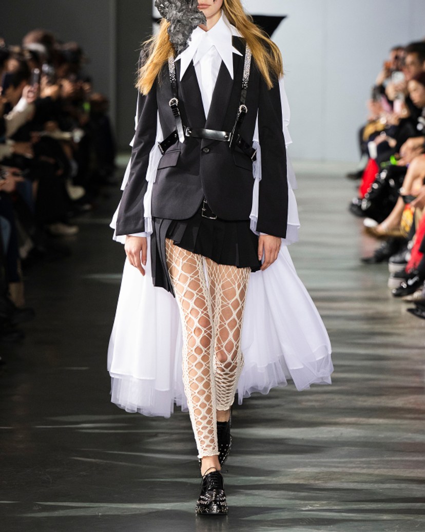 Runway look featuring black leather studded lace-up shoes worn with patterned leggings, a crystal-embellished harness and layered tailoring.