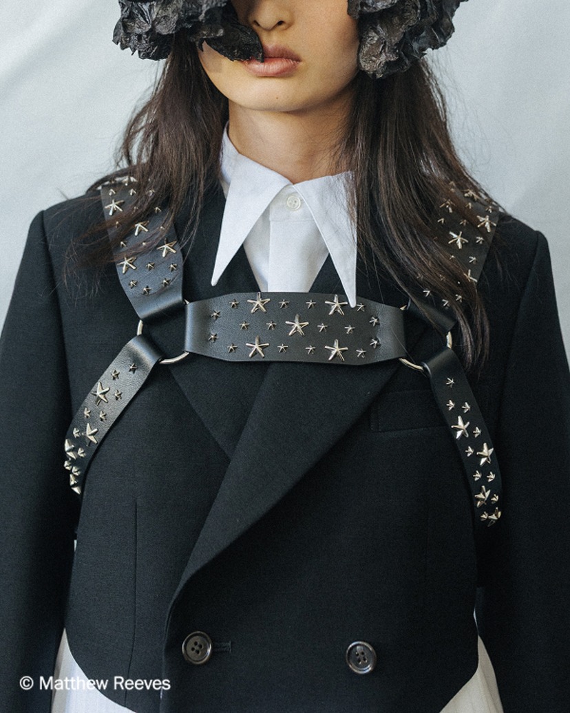 Close-up of a model wearing a black tailored jacket styled with a star-studded leather harness detail.