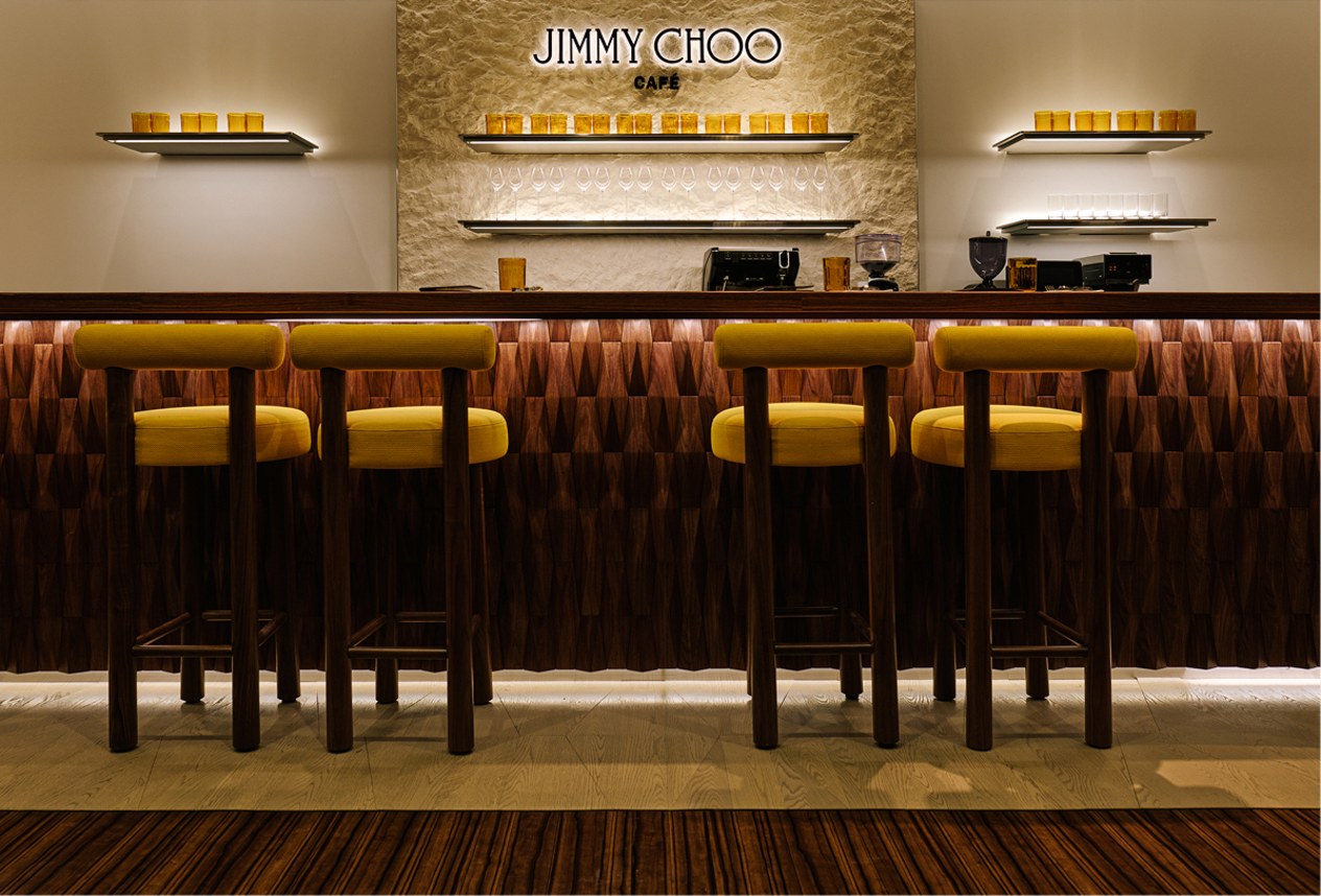 Jimmy Choo caf&eacute; bar with yellow stools and warm lighting.