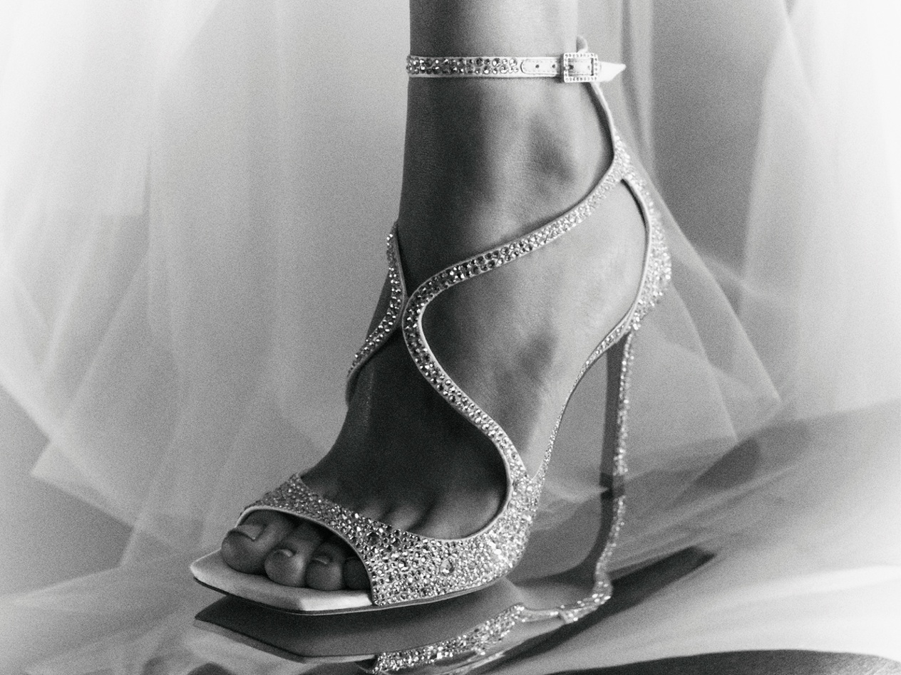 Black-and-white close-up of crystal-embellished heeled sandals with wraparound straps and mirrored reflection.
