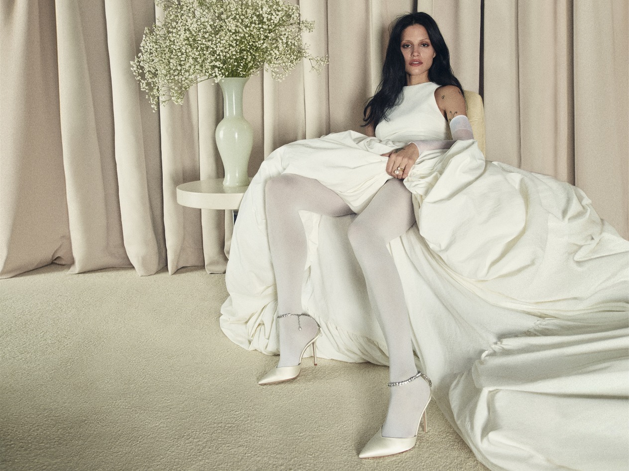 Model crouching in ivory dress wearing open-toe bridal heels and holding white flowers.	