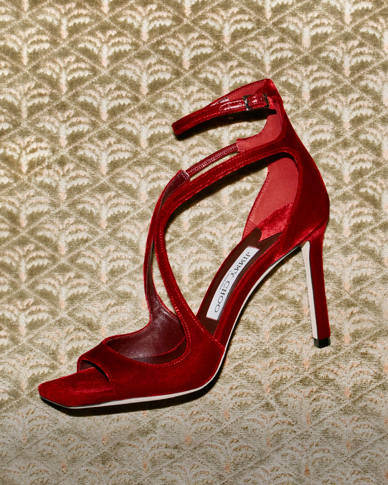 Red high-heeled sandal displayed against a patterned gold backdrop.