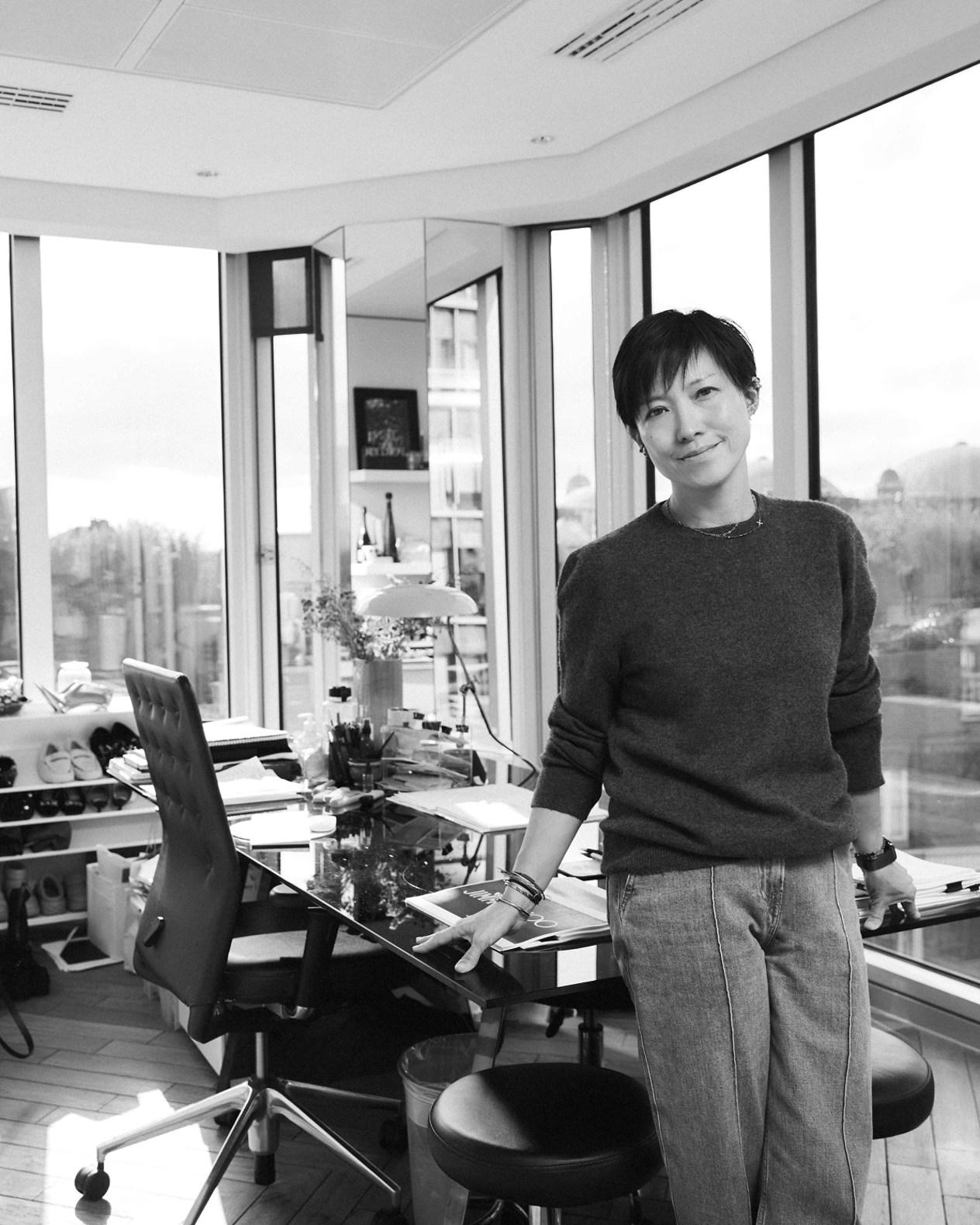 Black-and-white portrait of Sandra Choi standing in a modern office beside a desk, with floor-to-ceiling windows in the background.