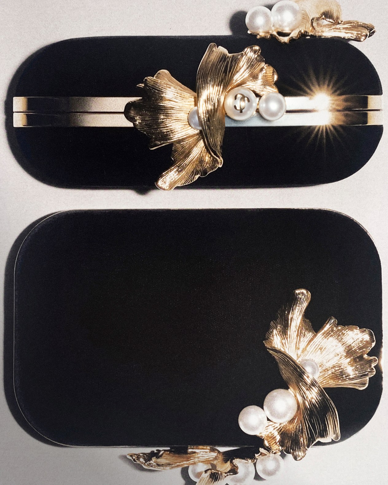 Black clutch bag with gold-tone frame, sculptural floral detailing and pearl embellishments, shown from two angles.