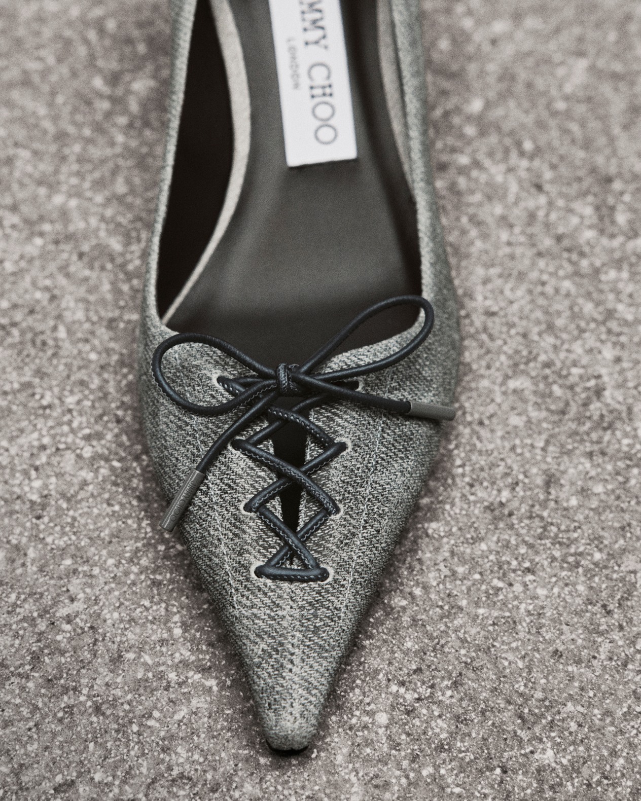 Grey pointed-toe fabric pump with corset detail, photographed from above on concrete.