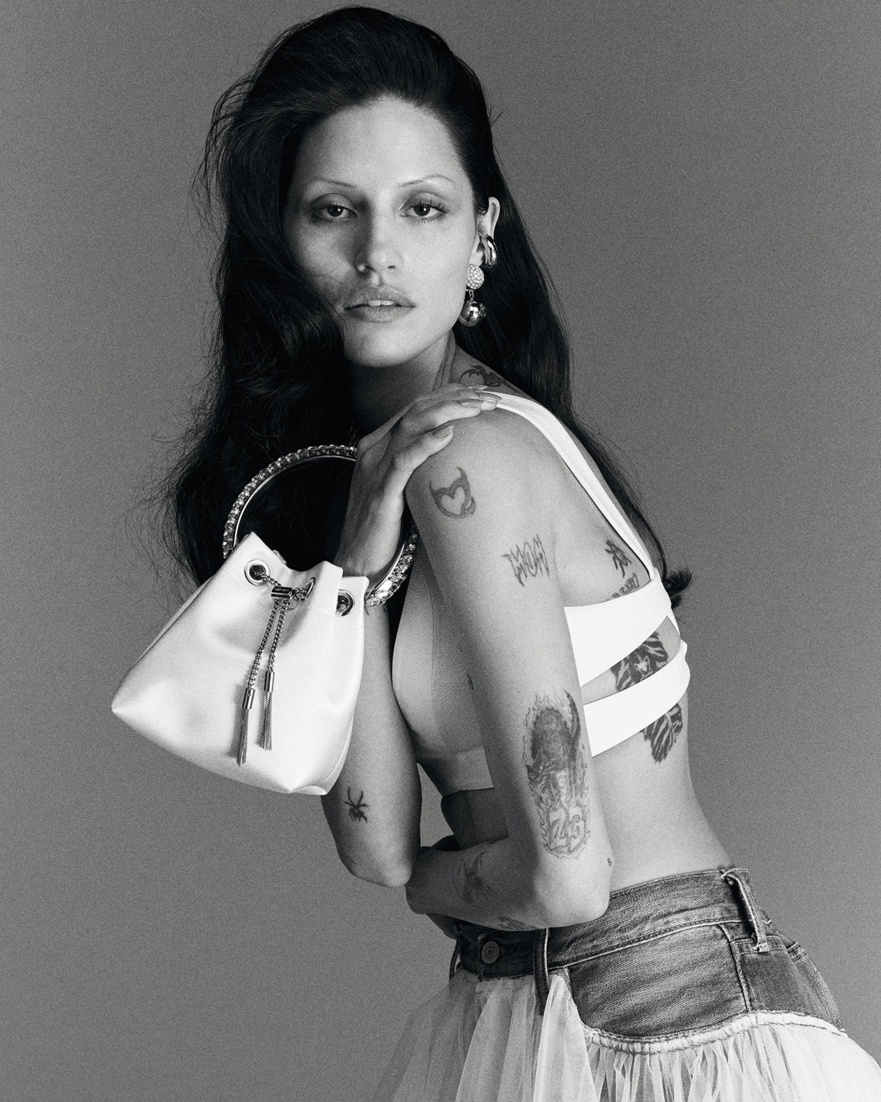 Tan leather top-handle bag with stud and pearl detailing, styled against green foliage.