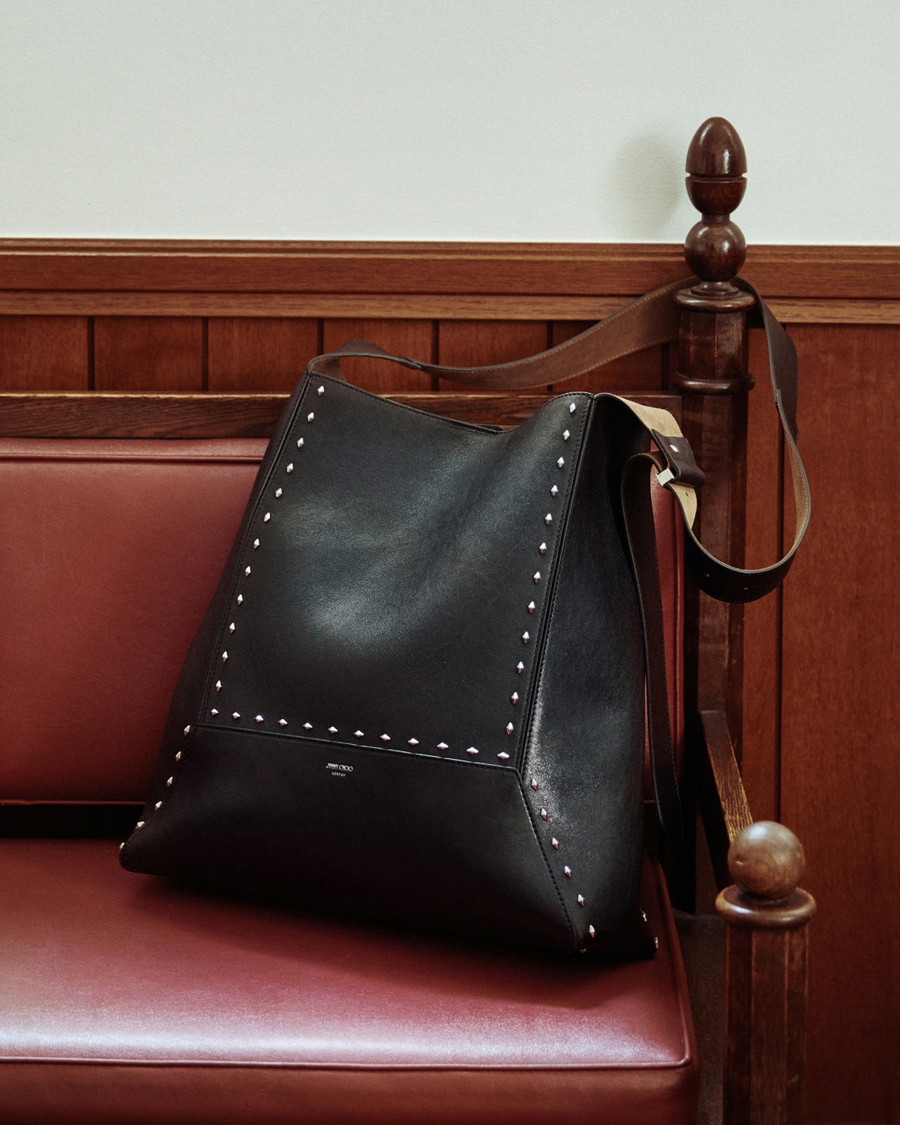 Black leather ankle boot with a mid block heel and sleek silhouette, displayed on a polished wooden chair with chrome details.
