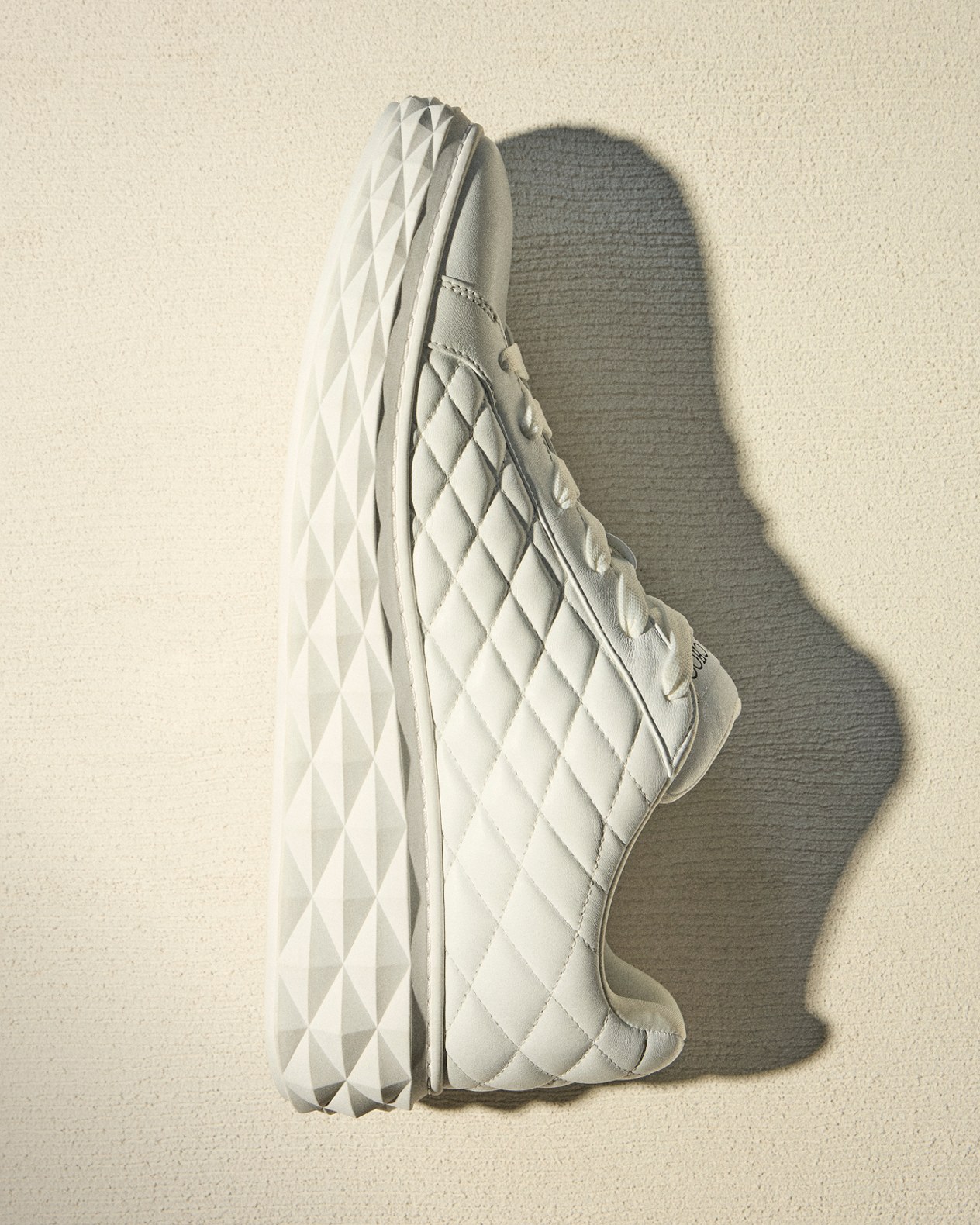 Side view of mens white quilted low-top trainers placed against a neutral background with shadow.