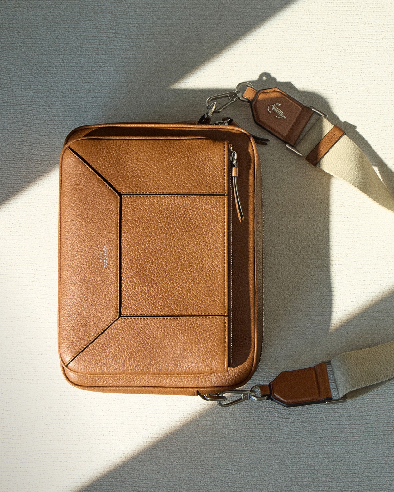 Mens leather crossbody bag with wide canvas strap, styled flat against a light background with shadows.