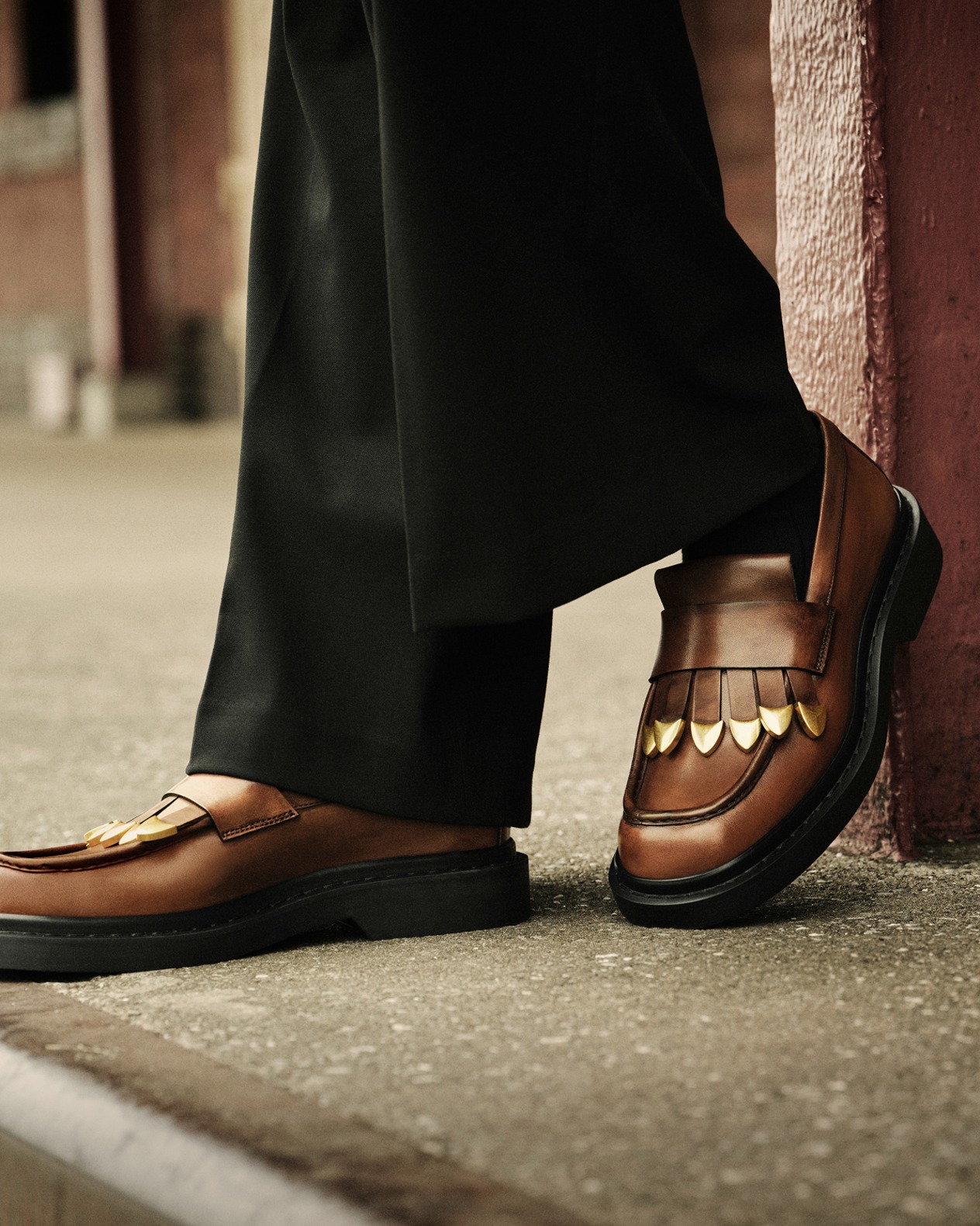 Close up of a male model wearing black trousers and brown leather loafers with fringe detailing.