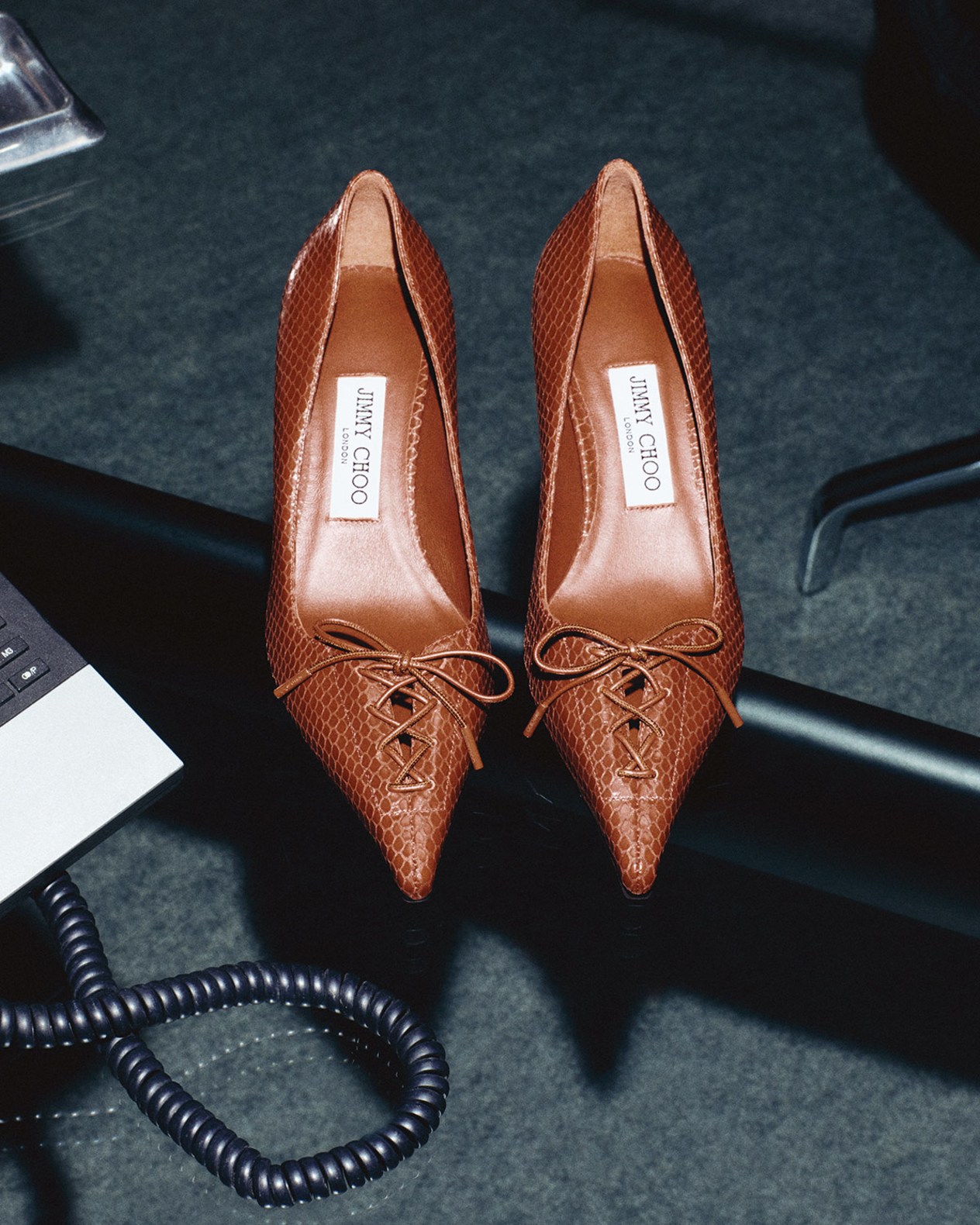 Brown snake print lace-up pointed-toe pumps placed side by side on a dark surface.