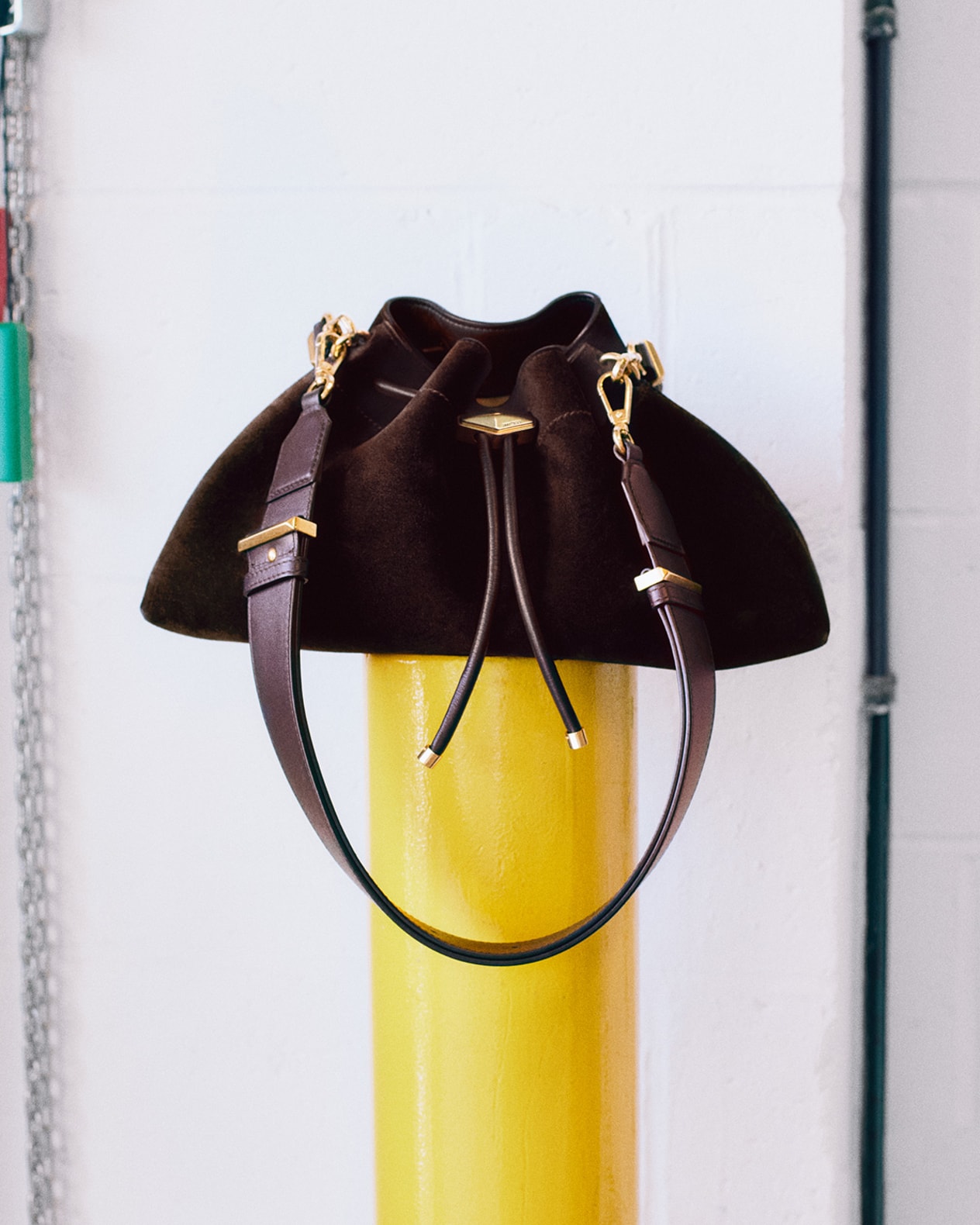 Brown bucket bag with gold hardware and a structured top handle, displayed on a yellow pole.