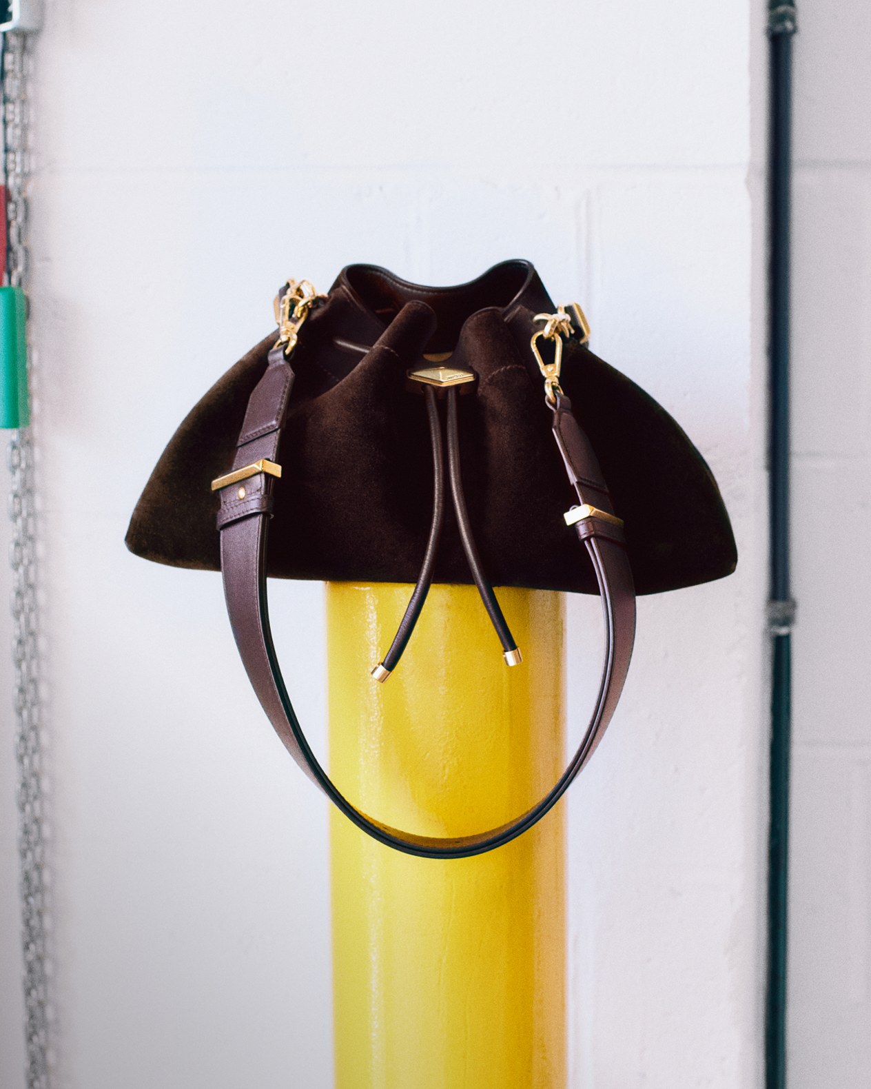 Burgundy leather drawstring handbag with a structured handle and gold hardware, displayed on a glass table.