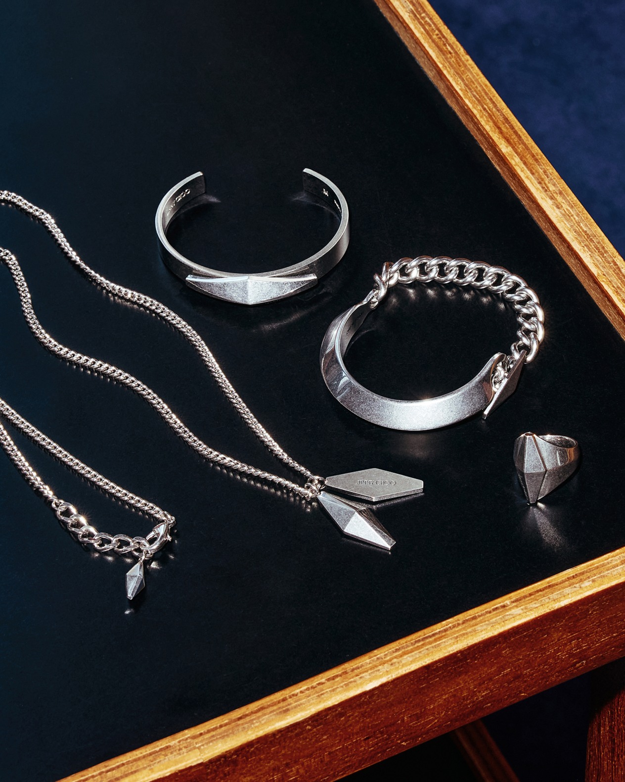 Selection of mens silver jewellery including bracelets, a ring and a pendant necklace displayed in a wooden frame case.