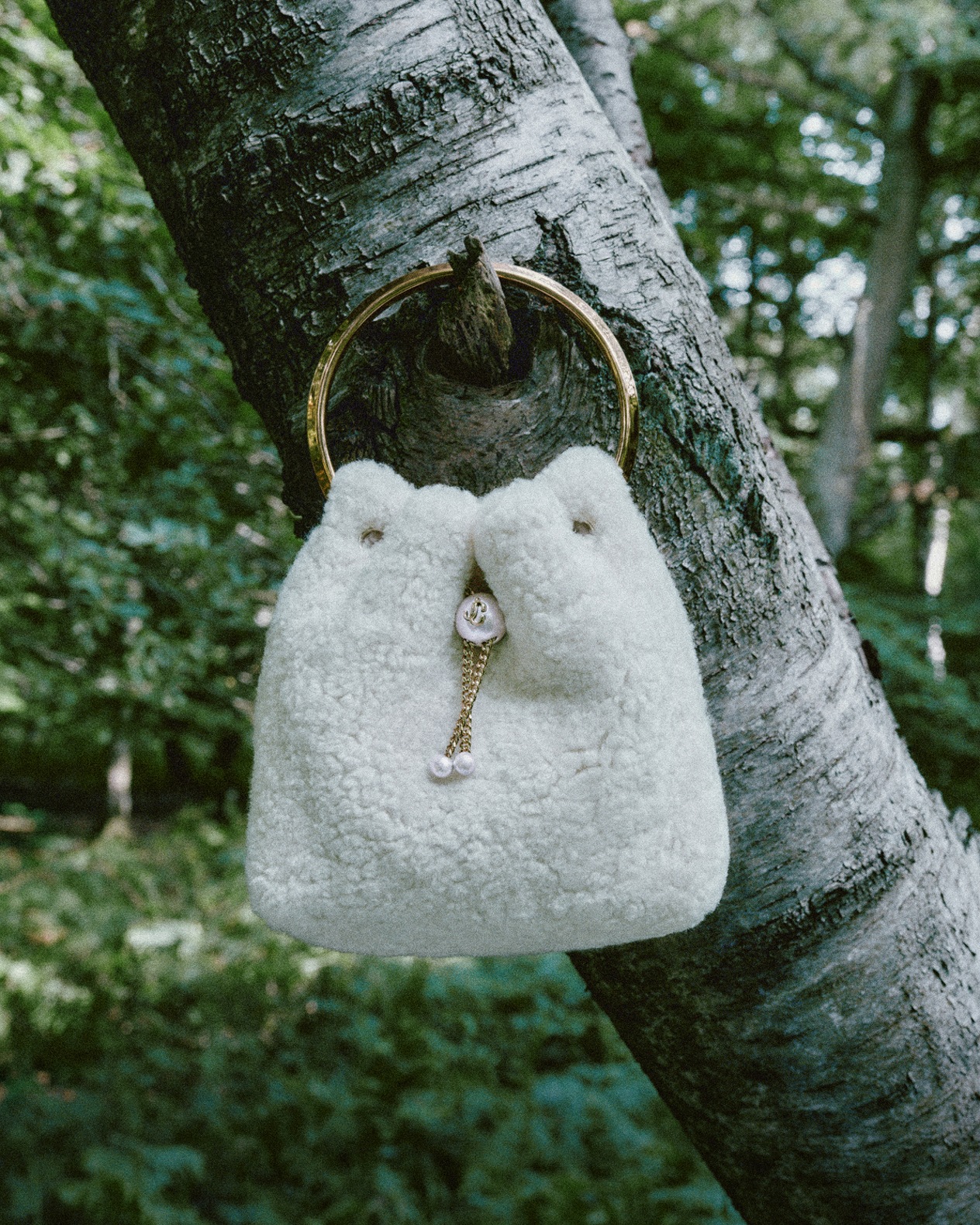 IMAGE ALT: Merlot leather drawstring bag with a gold chain and pearl detail, styled on a glass table.