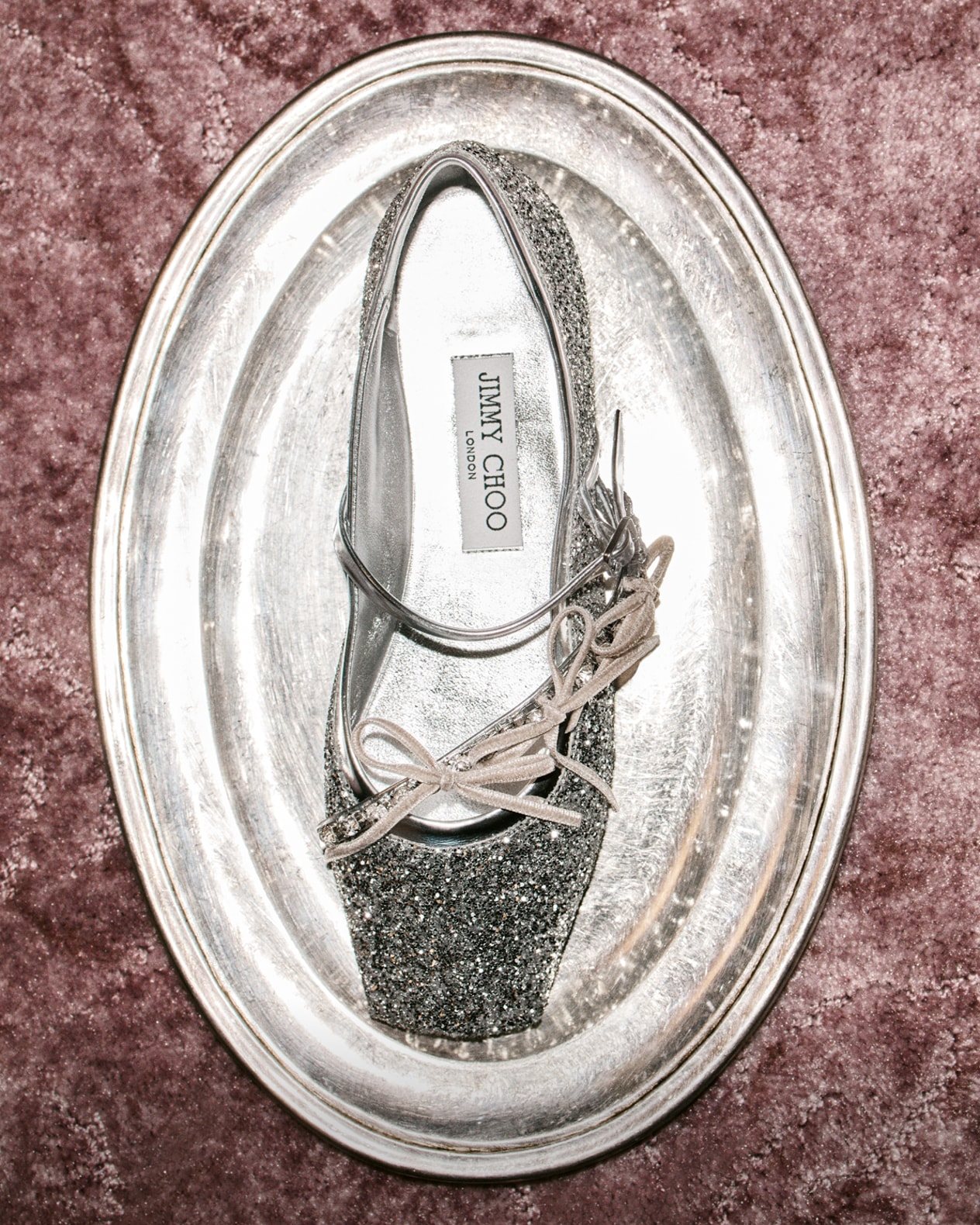 Woman, wearing leopard print heeled Eliot slippers styled with white socks, crouching to look through her bag, styled in a dark oversized sweater and photographed against a brick wall.