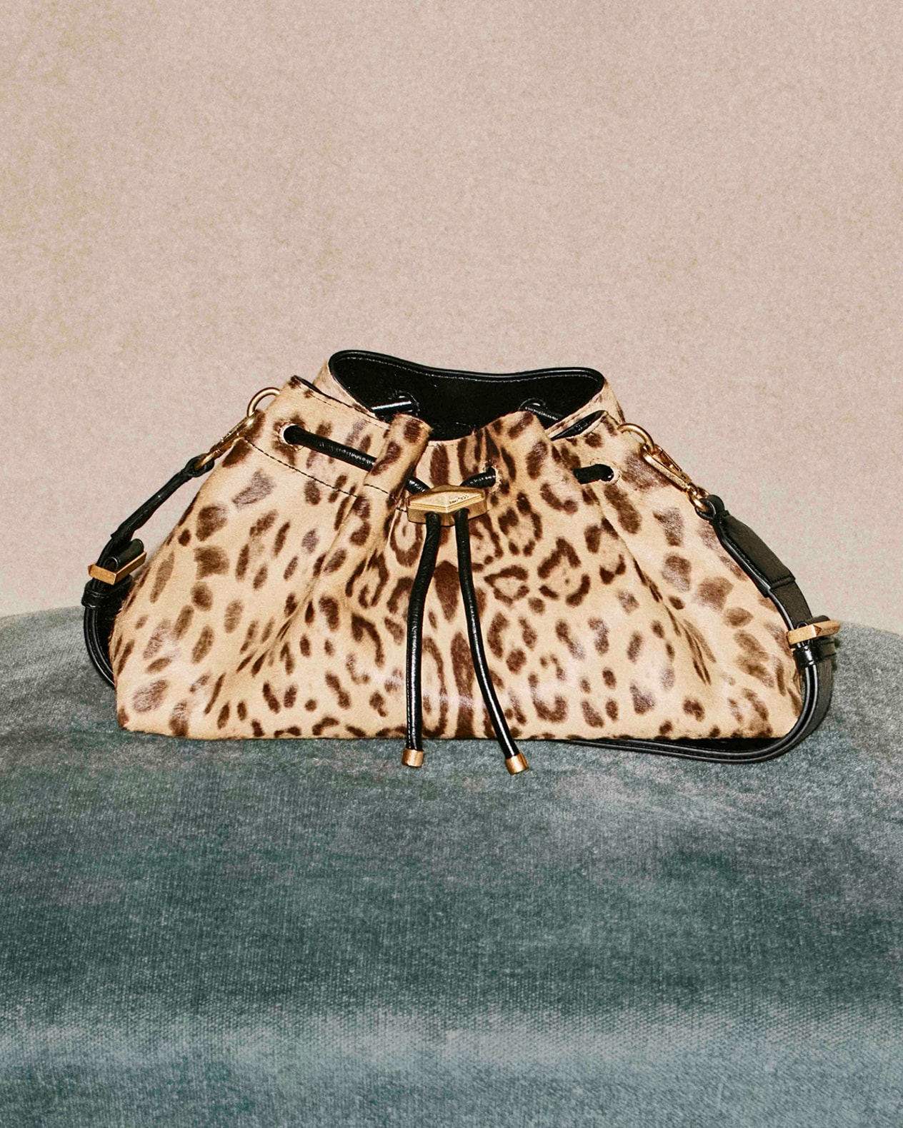 Leopard-print drawstring shoulder bag with gold hardware, photographed against a textured green surface.