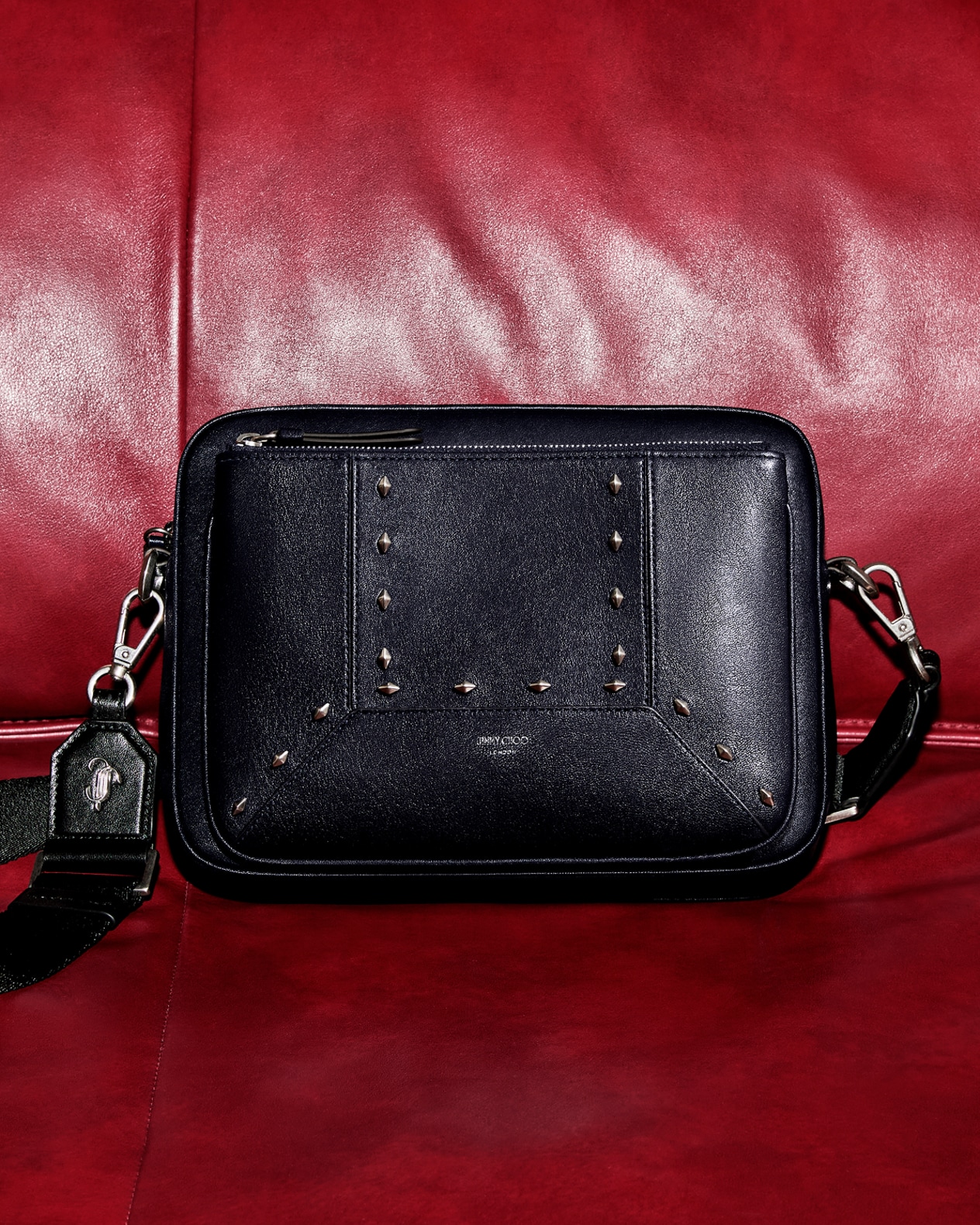 A pair of red satin pumps adorned with crystal bow embellishments, styled beneath a fringed throw.